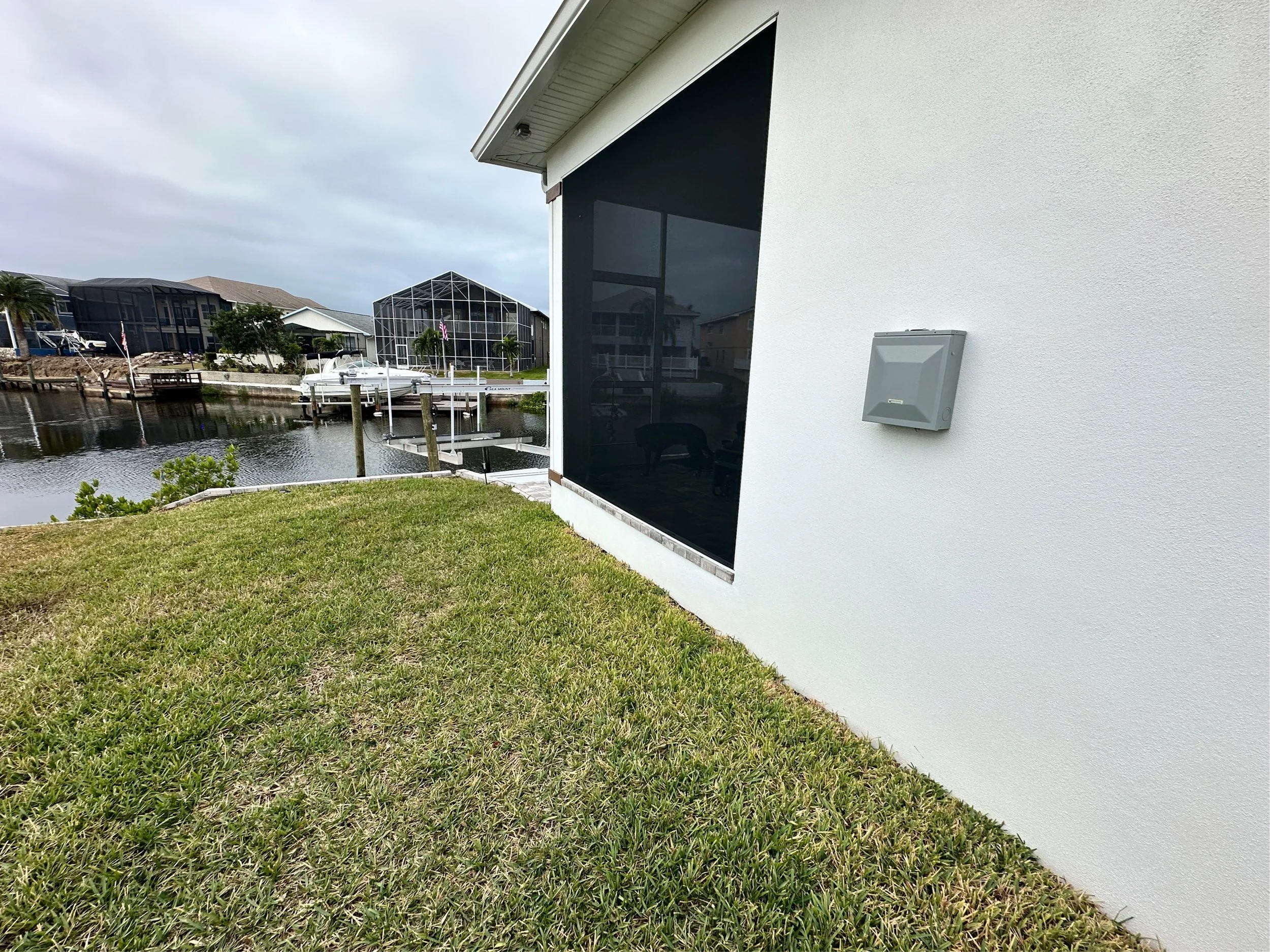 A white house with a screened porch overlooking a canal with boats and neighboring houses.