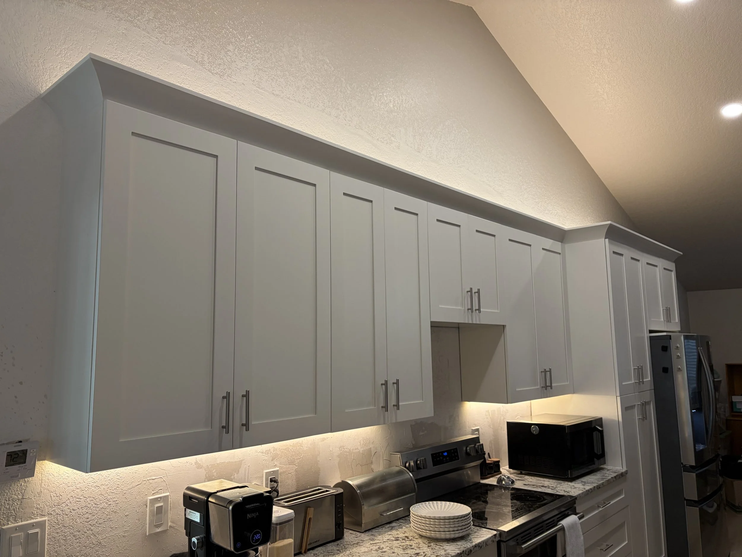 Kitchen with white cabinets, granite countertops, microwave, toaster, and refrigerator.