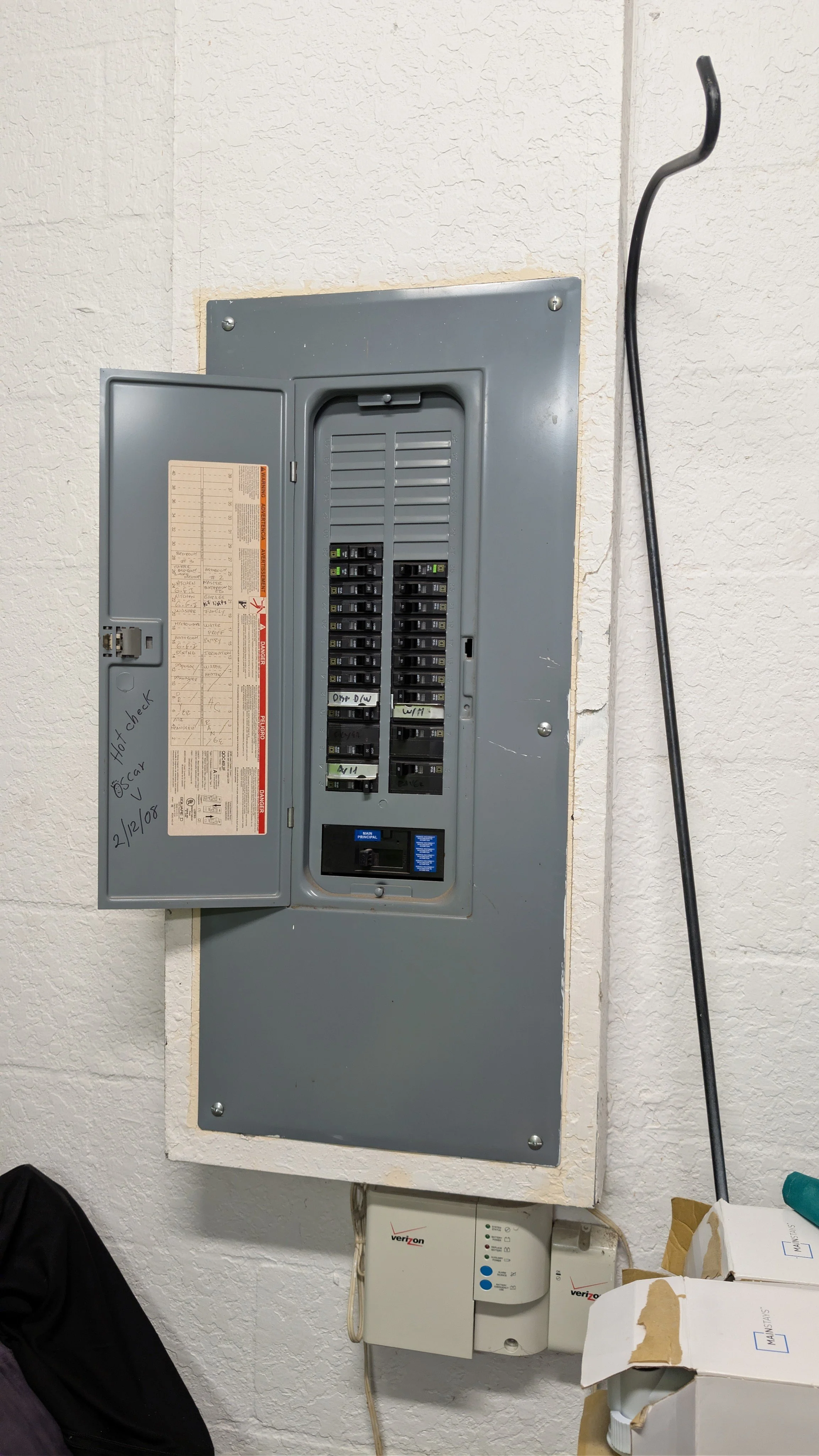 Electrical breaker panel with open door, handwritten notes, and a usable circuit breaker, mounted on a textured white wall.