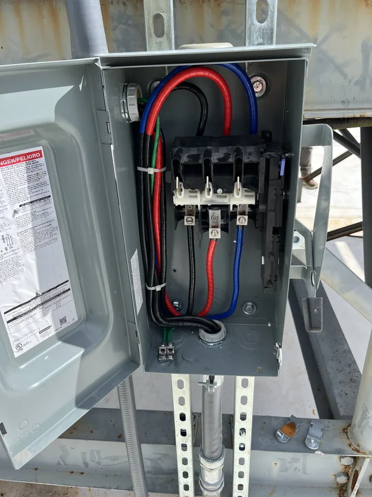 Open electrical panel with black, red, blue, and green wires, on a metal frame outdoor electrical box.