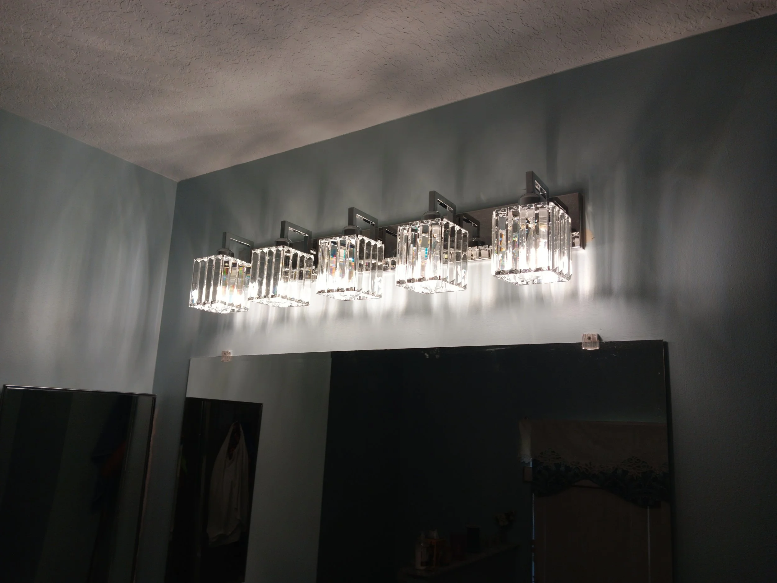 Five modern glass and metal wall-mounted light fixtures above a bathroom mirror.
