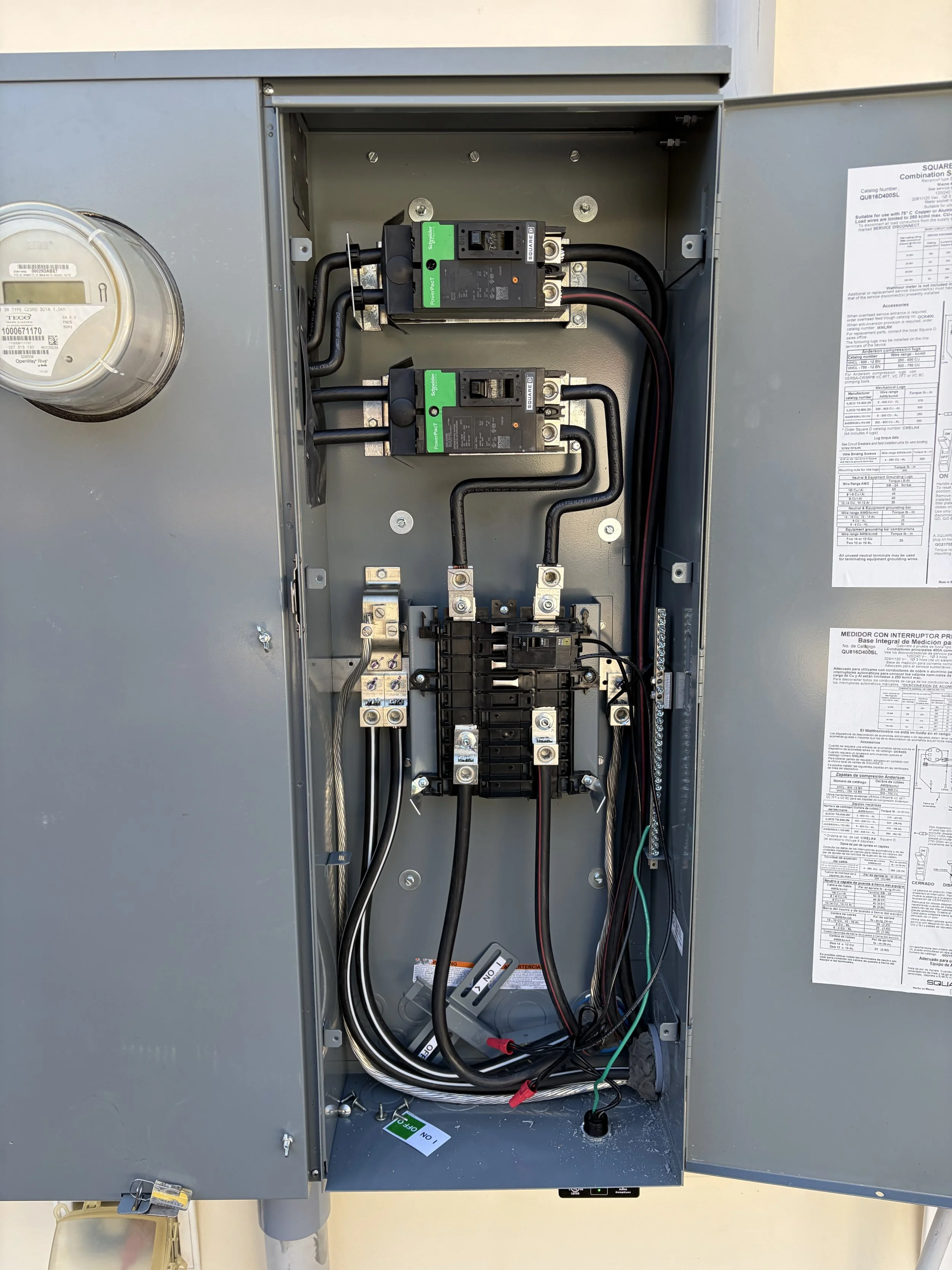 Electrical interior of a gray electrical panel with wiring, circuit breakers, and a power meter.