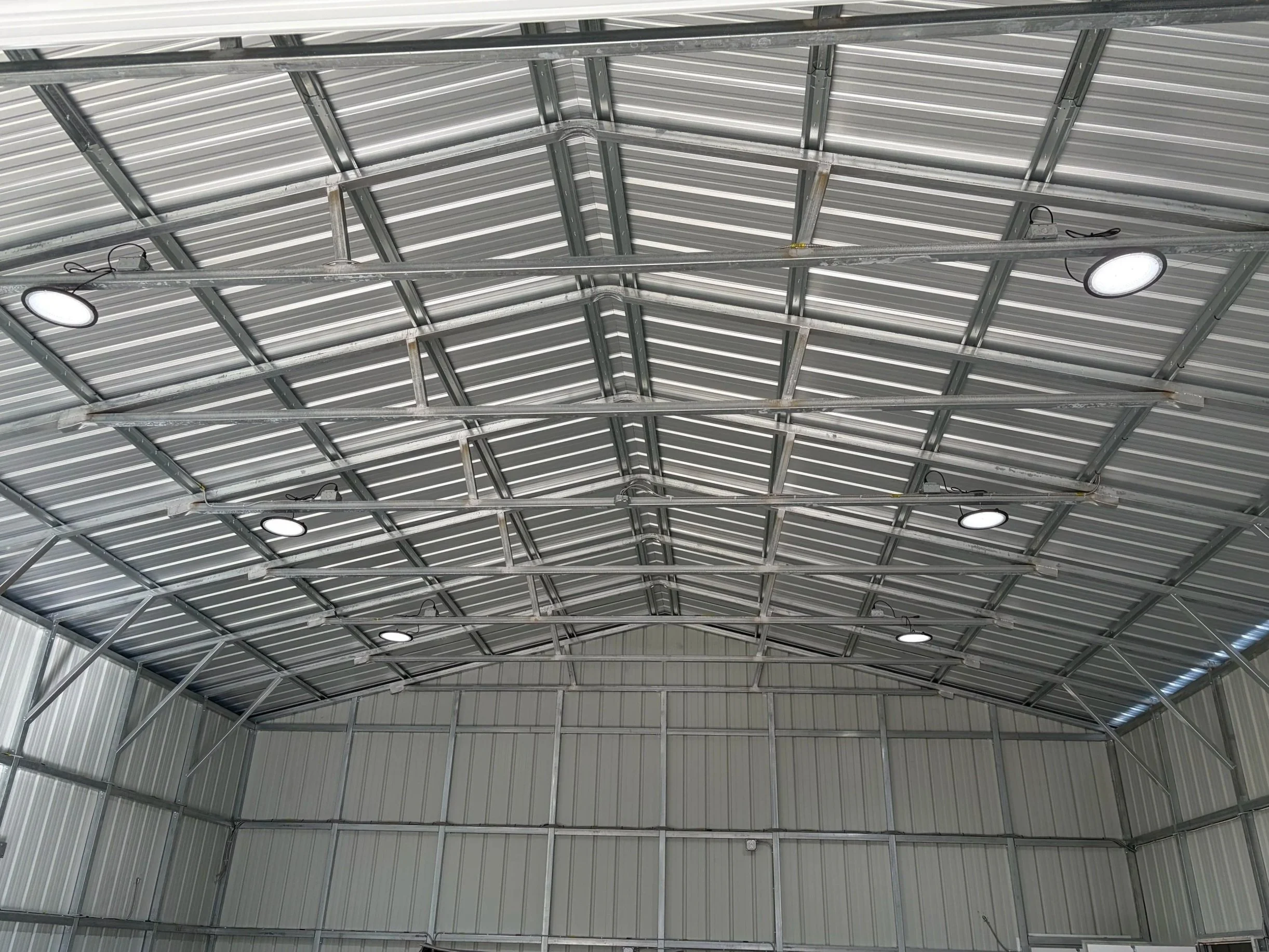 Interior view of a metal warehouse or storage building with metal roof and walls, illuminated by several ceiling-mounted LED light fixtures.