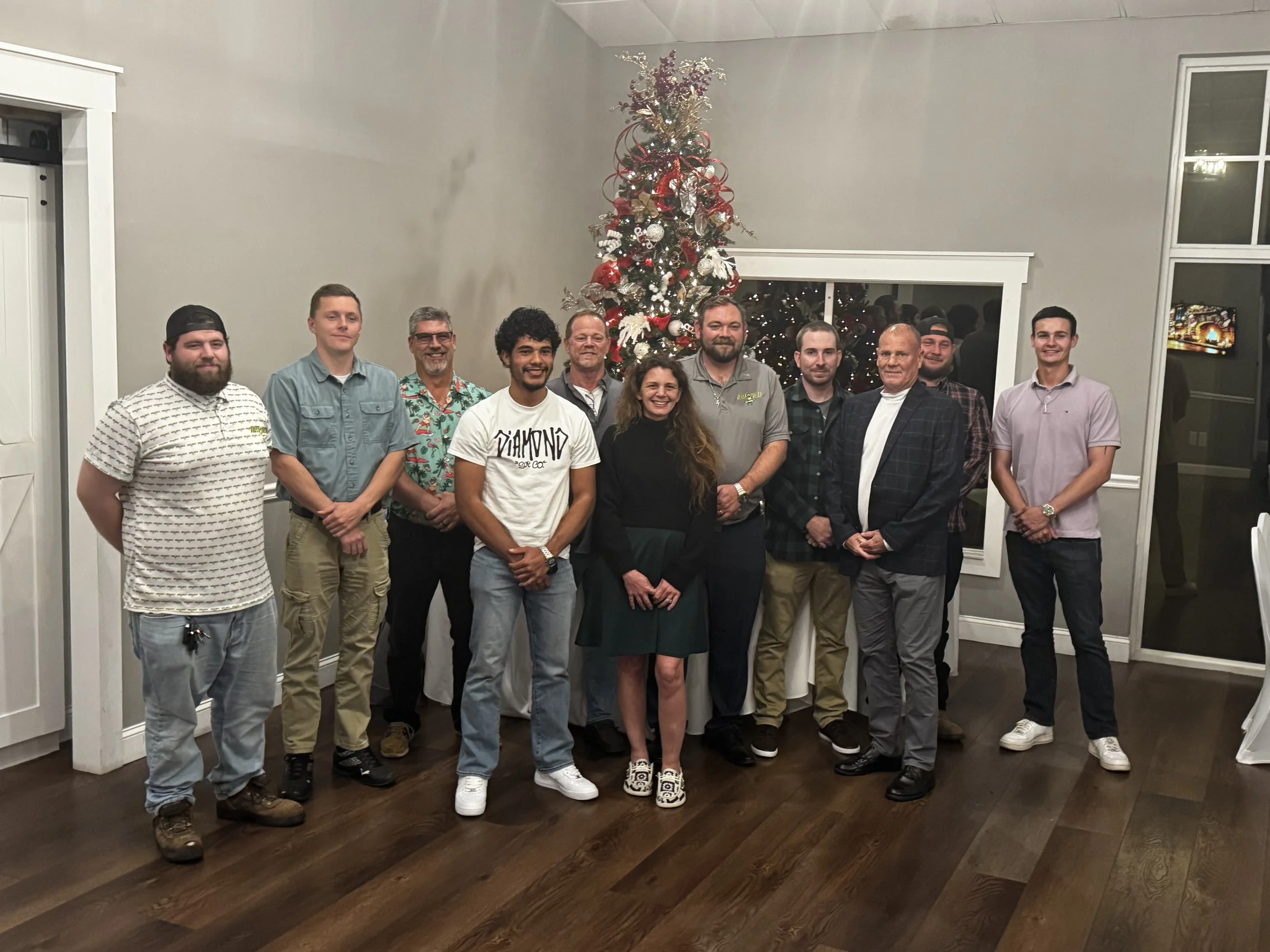 Group of people standing together in front of a decorated Christmas tree in a living room.