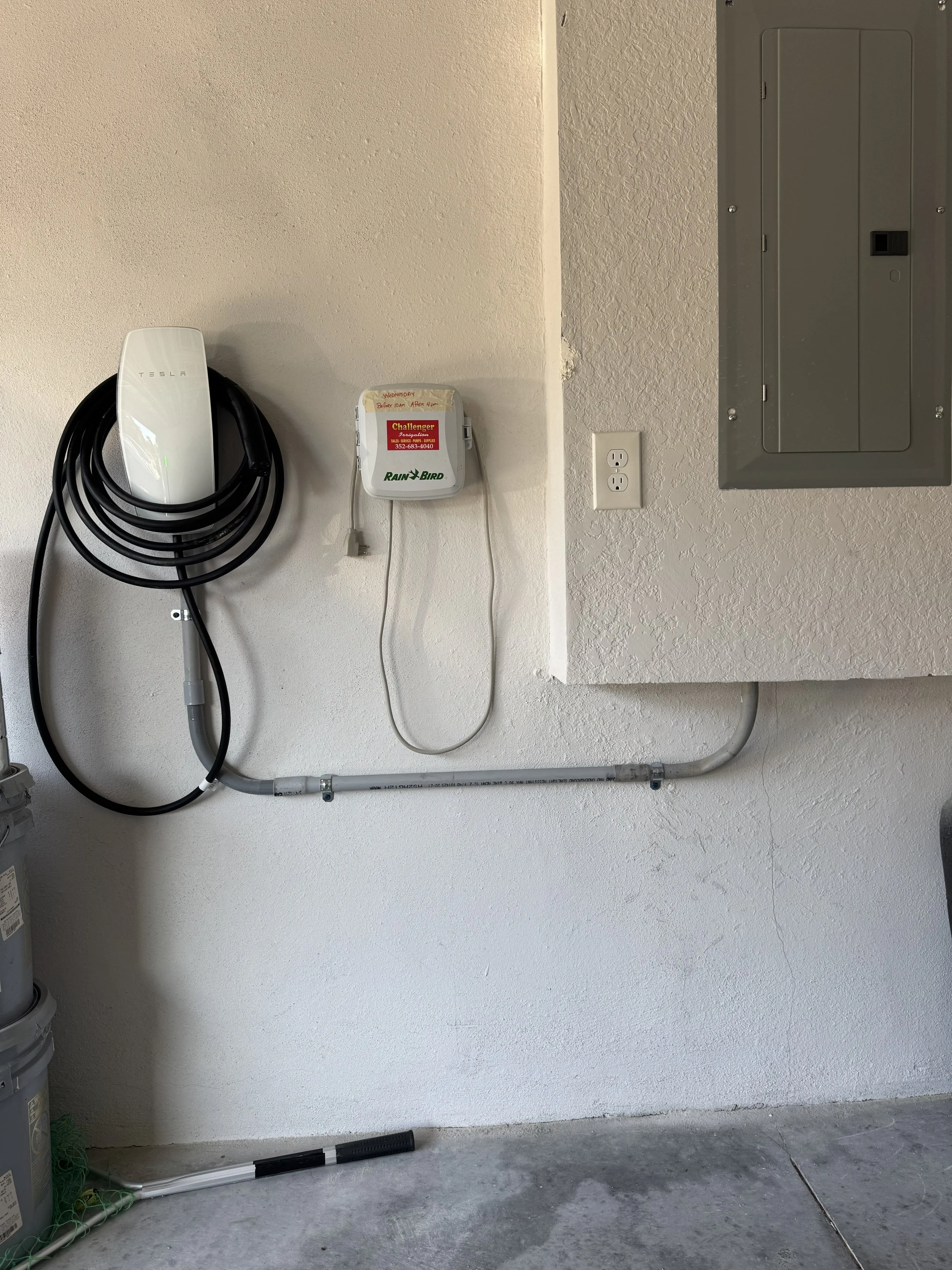 An electrical panel, an EV charging station, and a power outlet on a garage wall with conduit piping.