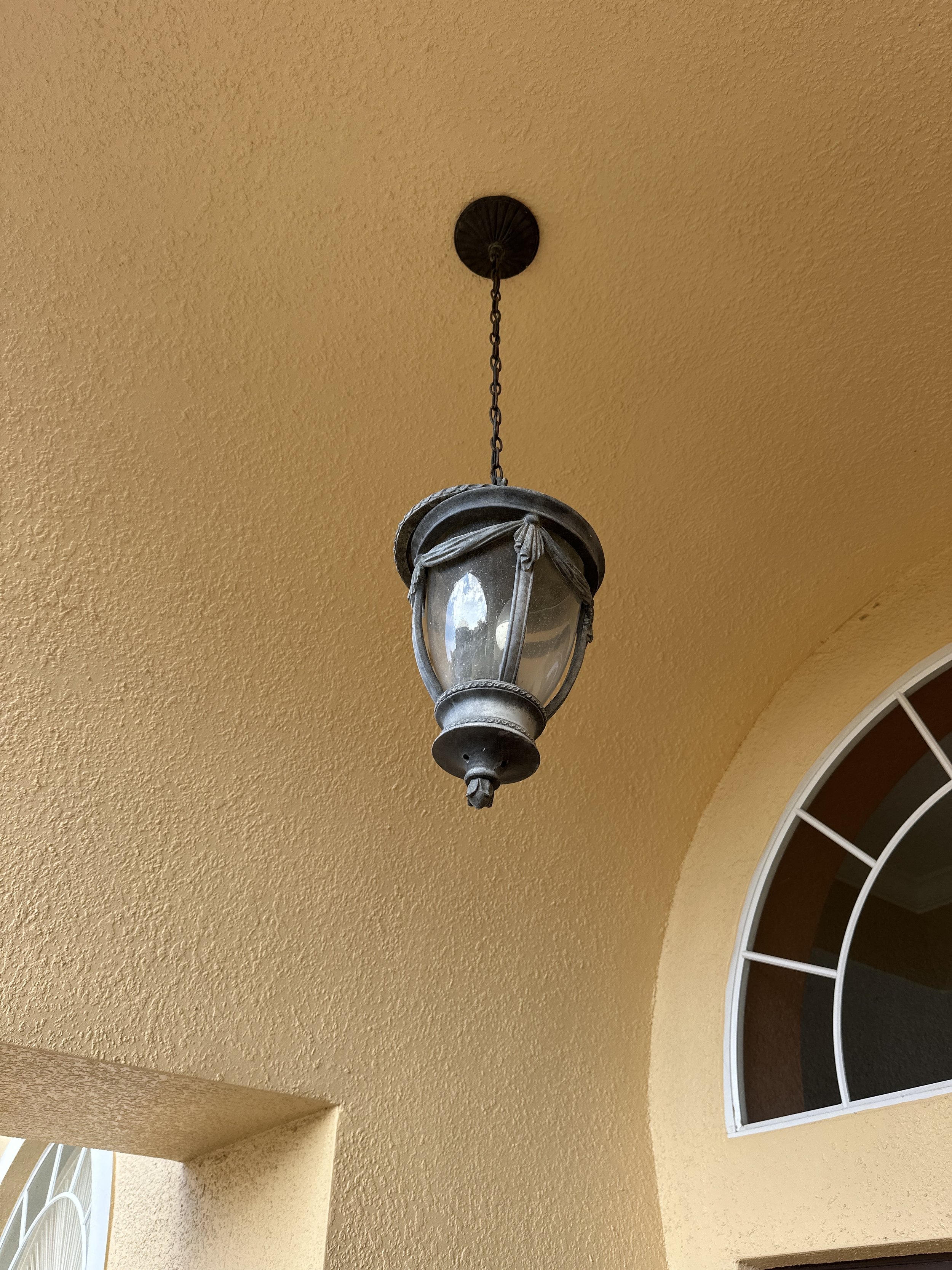 Outdoor hanging lantern light fixture on a yellow textured ceiling near a window.