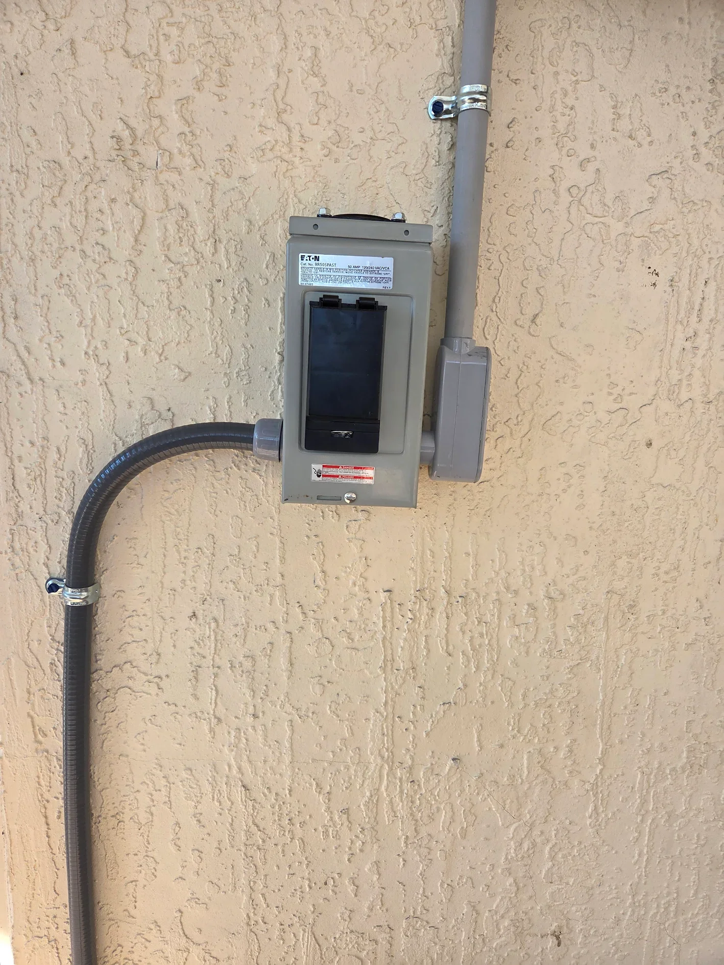 Electrical meter and conduit box mounted on a textured beige wall.