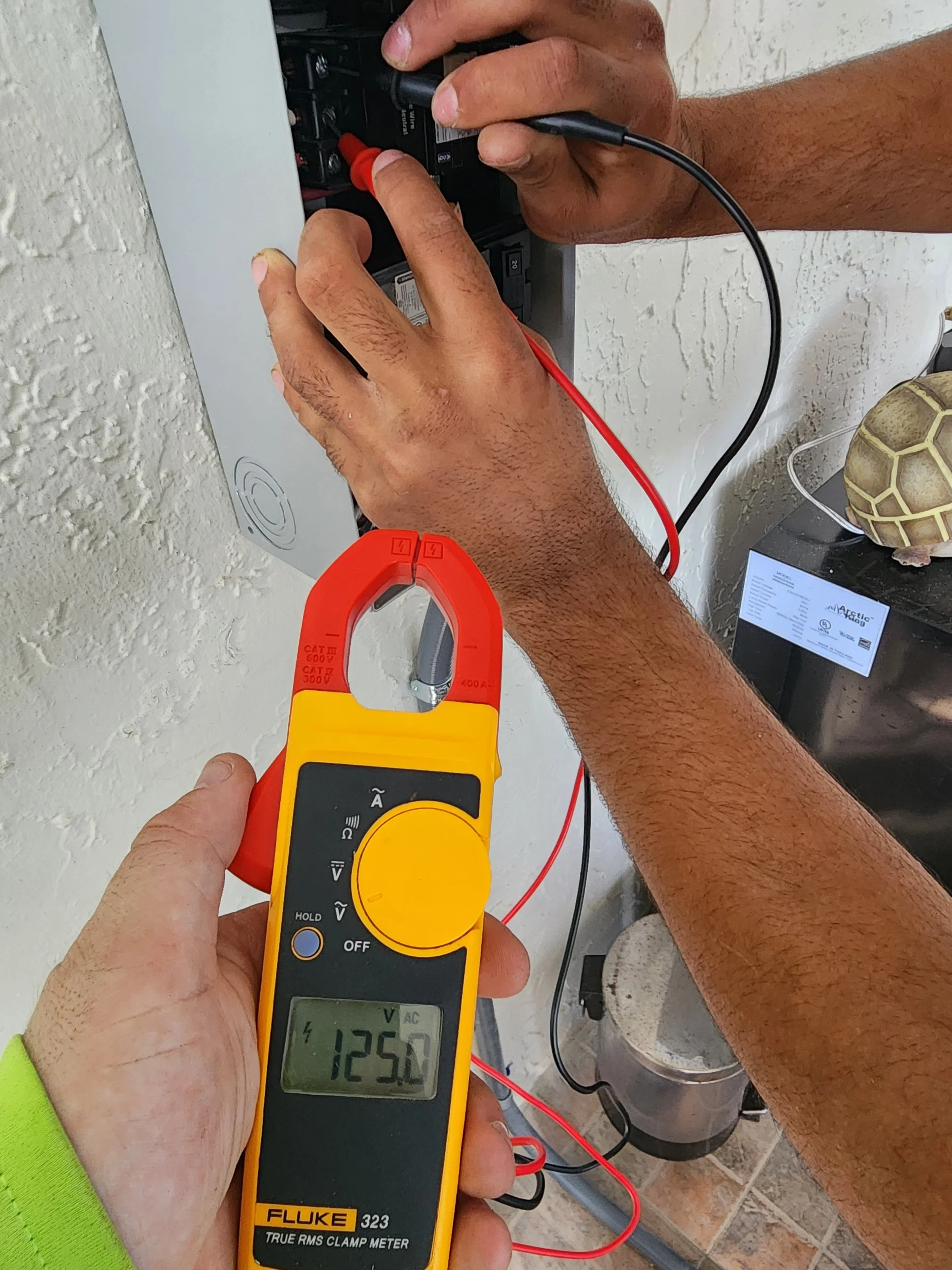 Person measuring voltage in an electrical panel with a multimeter, displaying 125.0 volts.