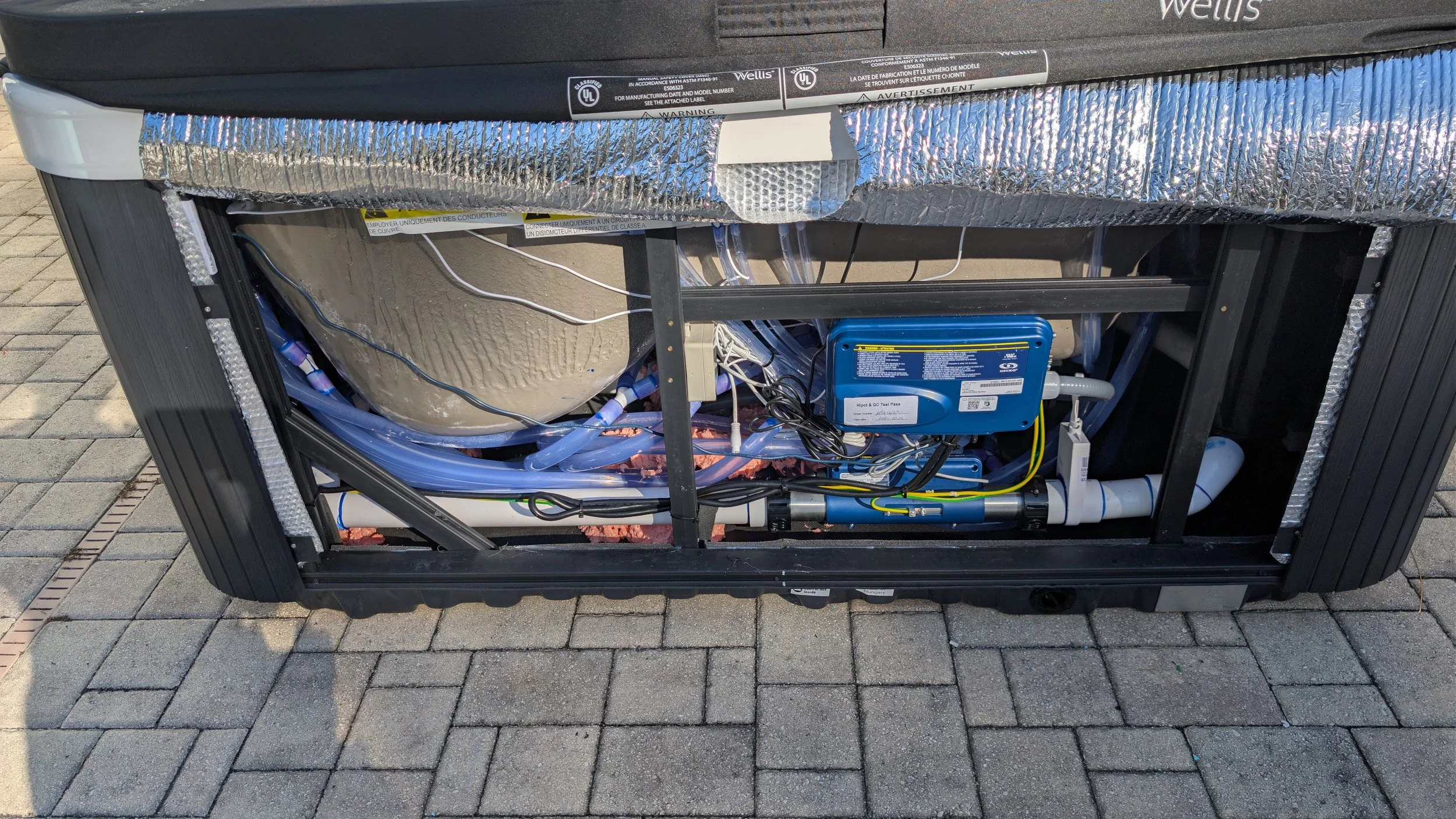 Open HVAC unit with visible wires, tubes, and a blue control box, situated on a brick surface.