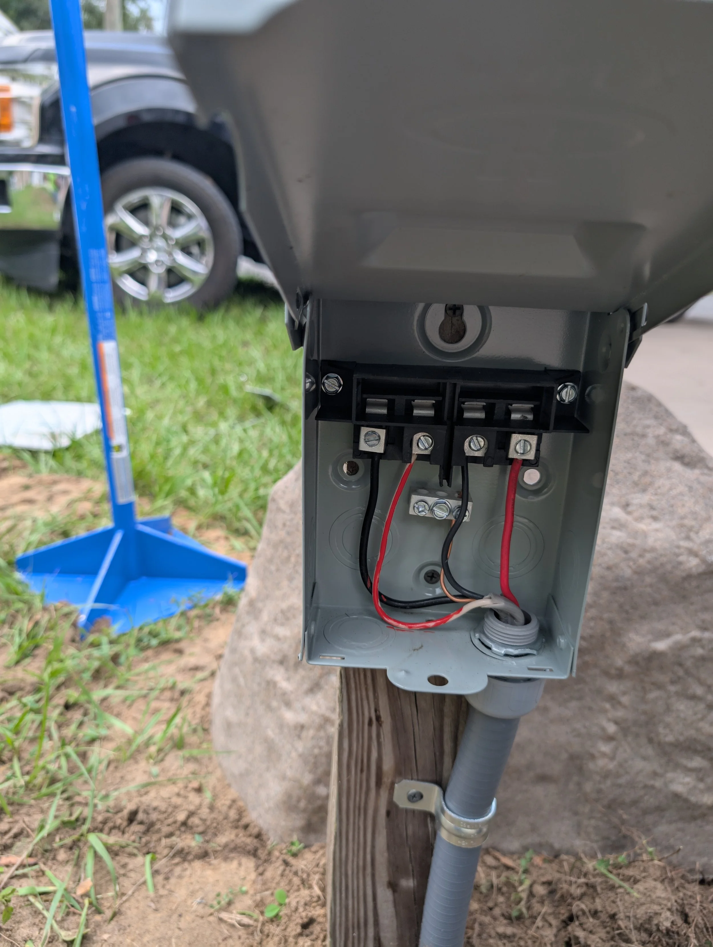 Open electrical box mounted on a wooden post, showing wires and connectors inside.
