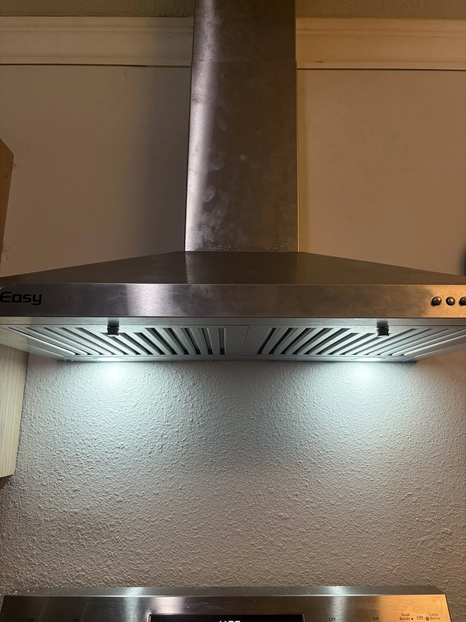 Stainless steel kitchen range hood with vents and control buttons, mounted on a textured wall.