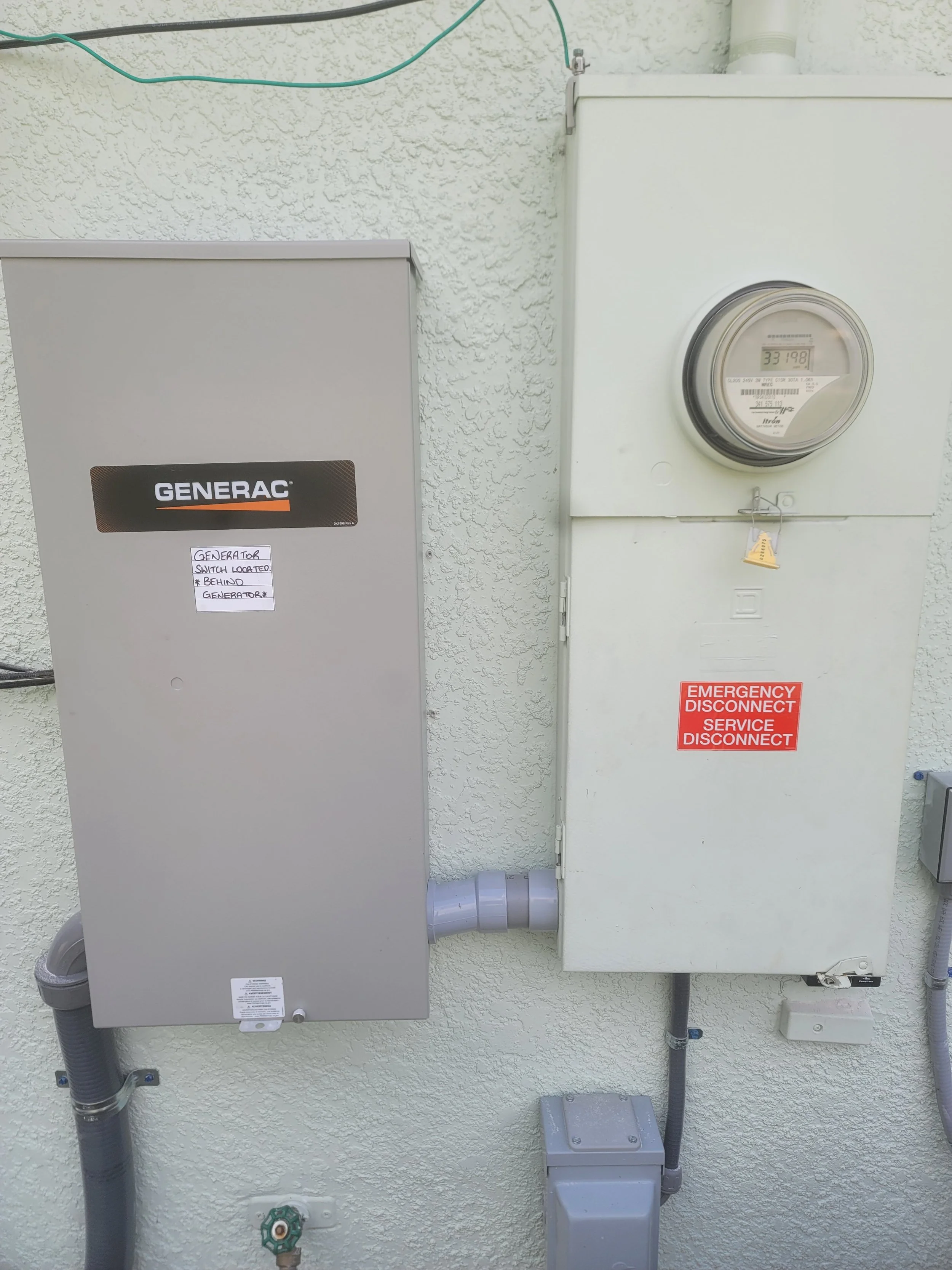 An external wall with a generator and an electric meter, with signs indicating generator switch location and emergency disconnects.