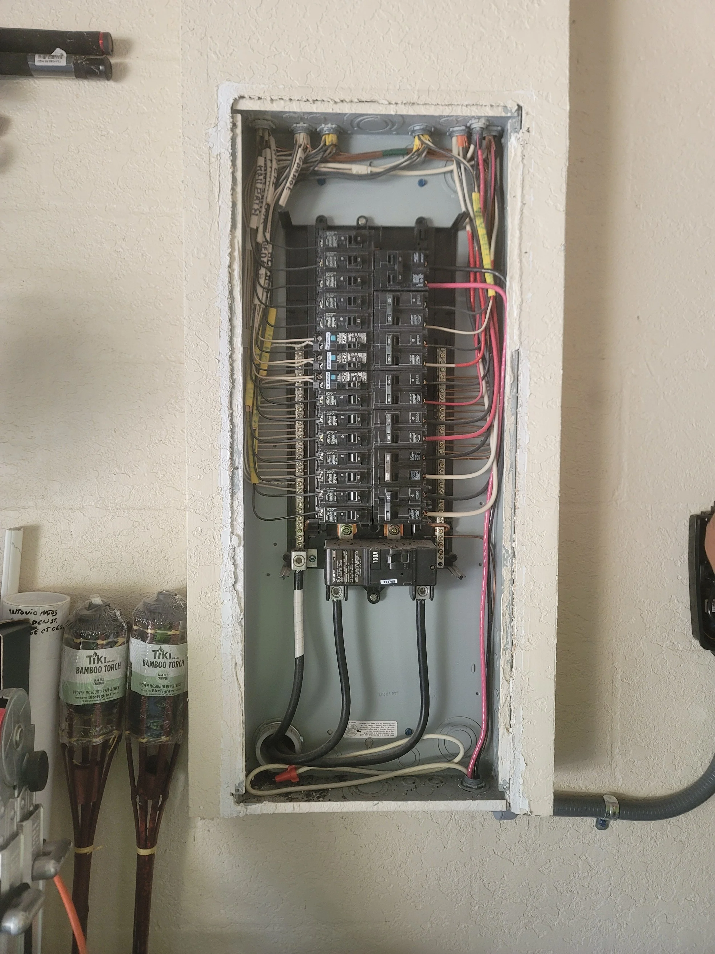 An open electrical breaker box with multiple circuit breakers and wiring inside, mounted on a wall.