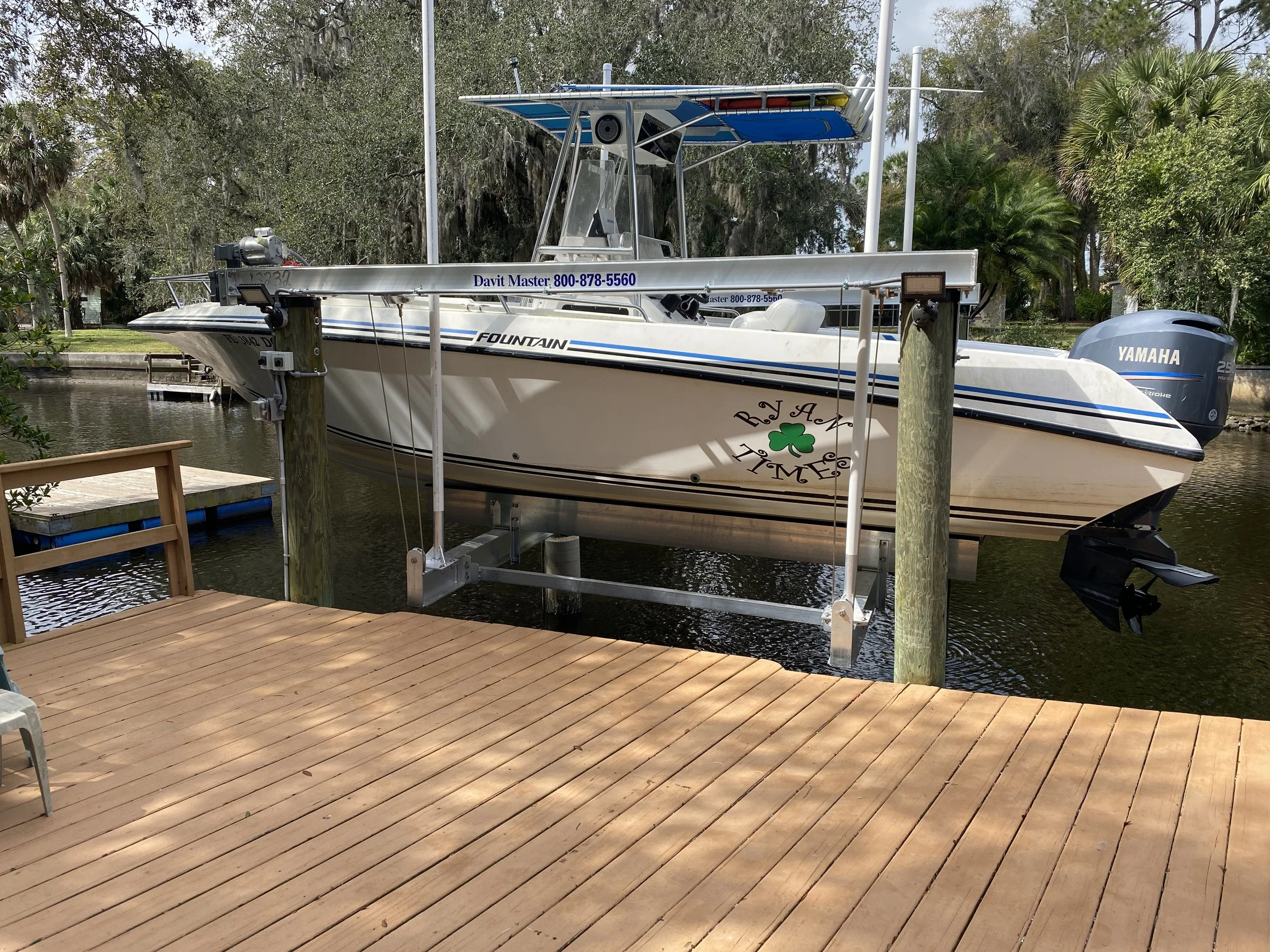 A motorboat is docked at a wooden pier, with a Yamaha outboard motor at the stern, an outboard engine on the water, and surrounding trees in the background.