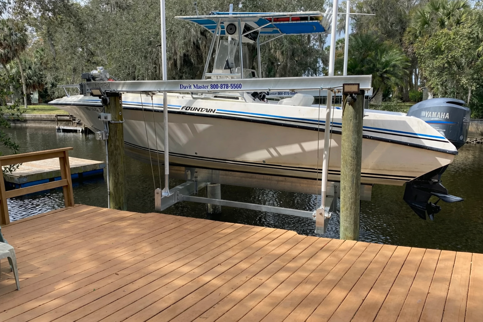 A white Fountain boat with a Yamaha outboard motor is docked at a wooden pier on a waterway, surrounded by greenery.
