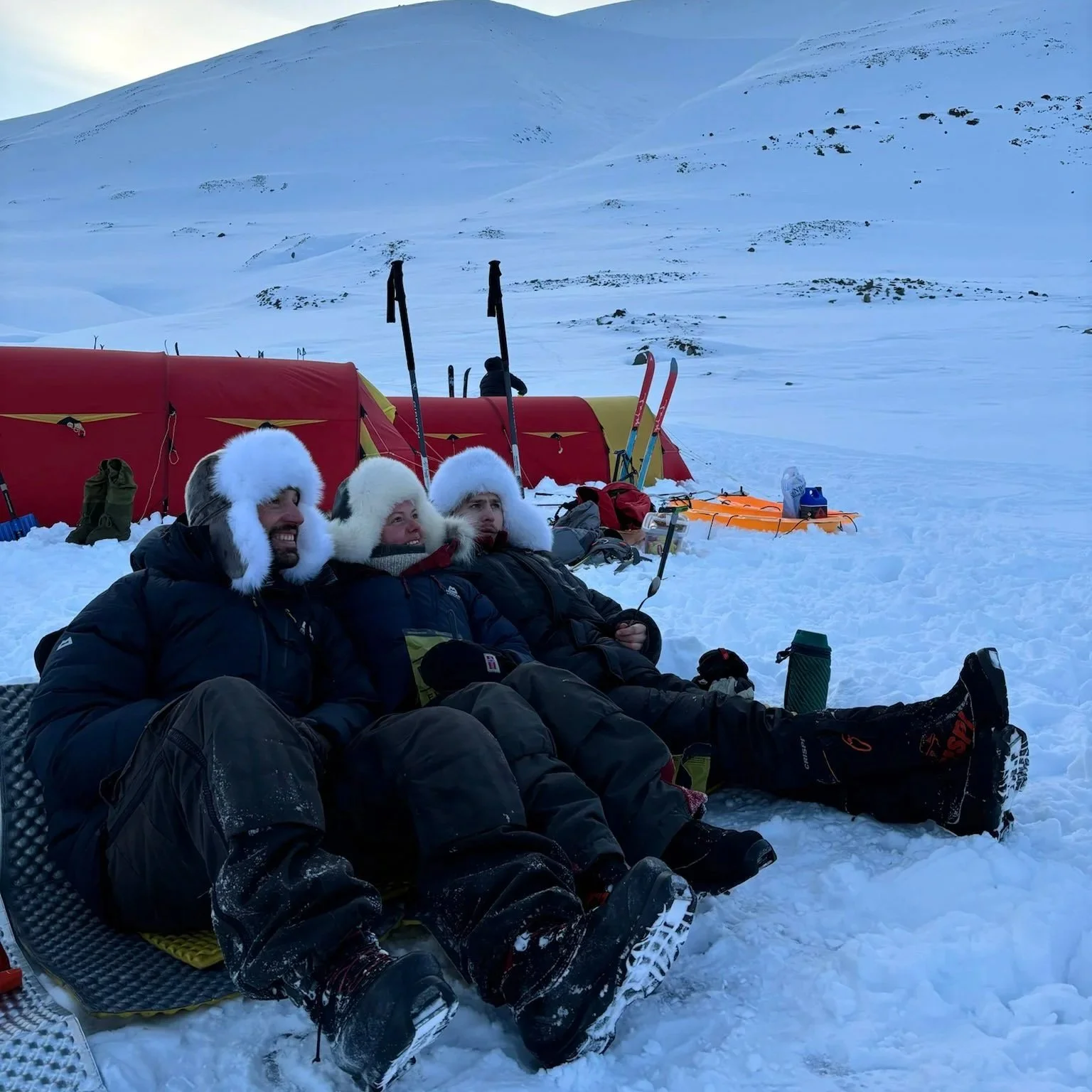 Tre personer som sitter i snøen og smiler