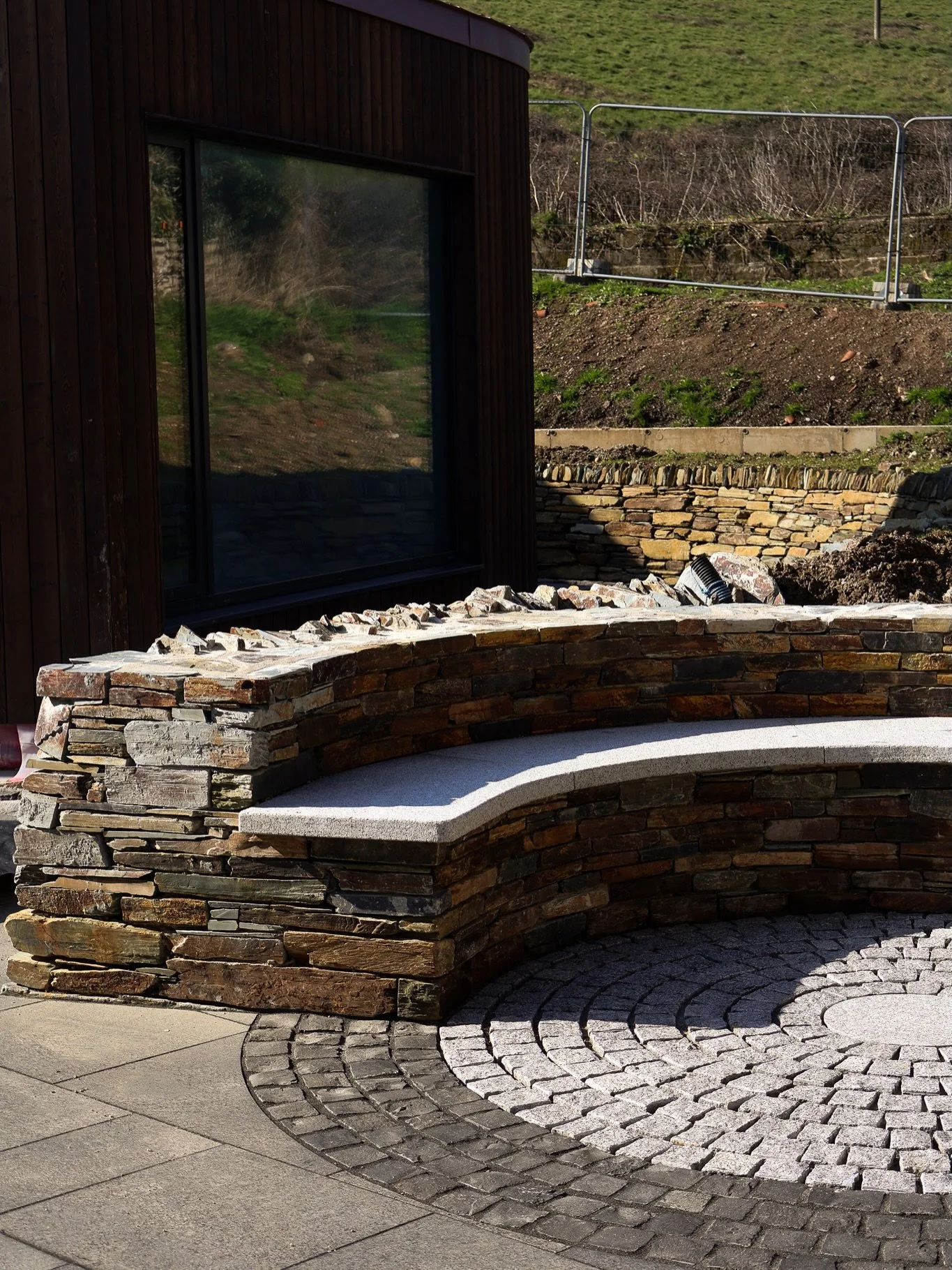 The new fire pit is now complete, designed with a dual function: creating a defined seating area while also retaining water to protect the house during heavy rainfall.

Seating has been carefully crafted from 50mm thick granite and setts, arranged in