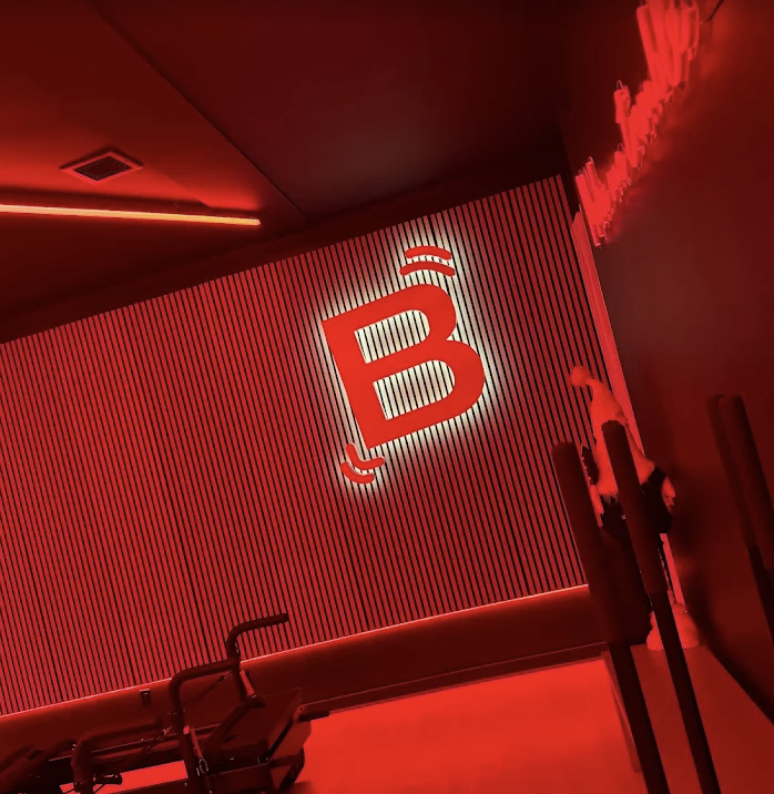 Red-lit room with a large illuminated sign featuring a 'B' with Wi-Fi signals on top, and a lounge chair beneath it.