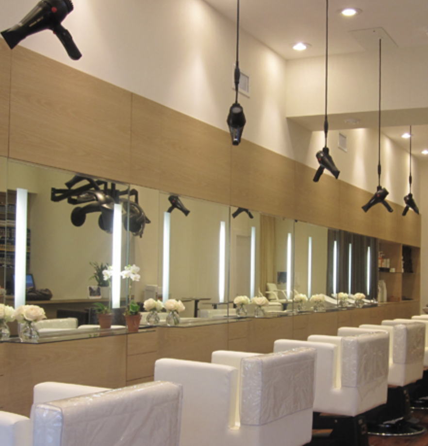 Salon or beauty parlor with styling chairs, mirrors with lights, and hairdryers hanging from the ceiling.