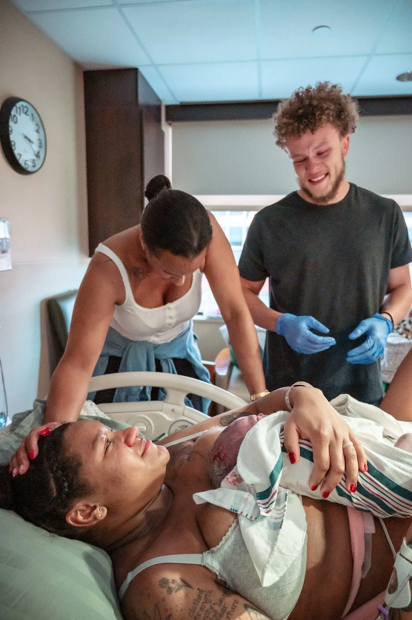 Woman lying in hospital bed holding a newborn baby, with a woman and a man beside her, in a hospital room.