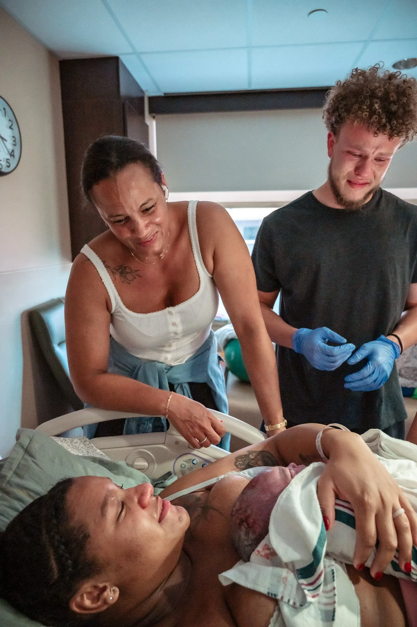 A woman giving birth in a hospital with a man and a woman present, all visibly emotional.