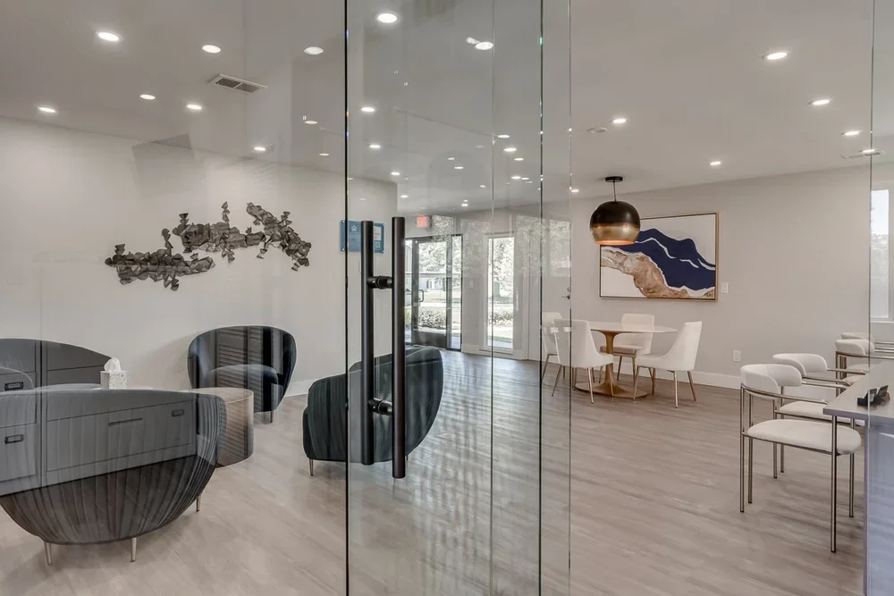 Modern, minimalistic lounge with black chairs, a gray sofa, wall art, and a dining area with white chairs and a copper hanging pendant light.