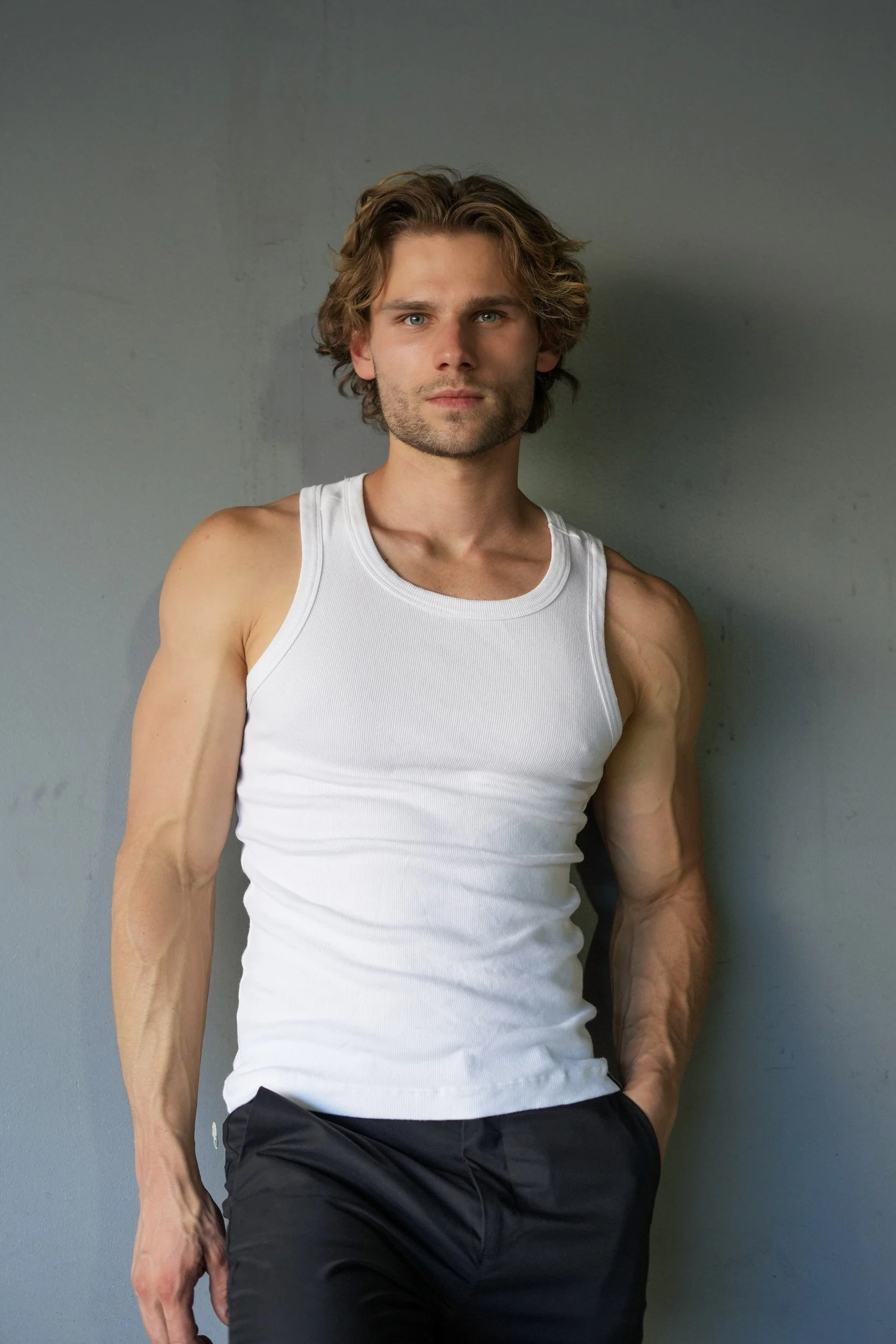 Stepan Salomatin standing in a white tank top against a gray wall