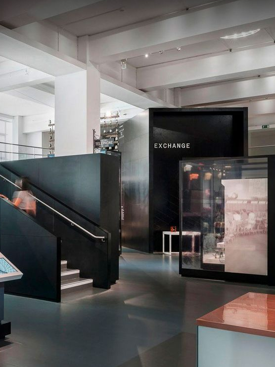 Interior of a modern building with black walls, stairs, and signage indicating a currency exchange area.