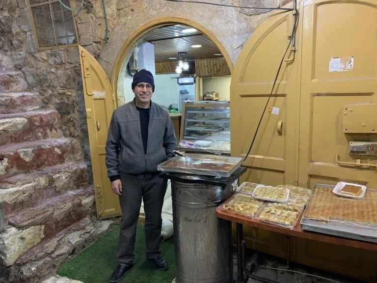 Ramez Za’Atari stands outside of his sweet shop in Al-Khalil’s old city on November 16, 2025. Despite seeing few visitors and the threat from Israeli settlers, Za’Atari opens his shop every day to keep his store alive. PHOTO: Giancarlo Cininni