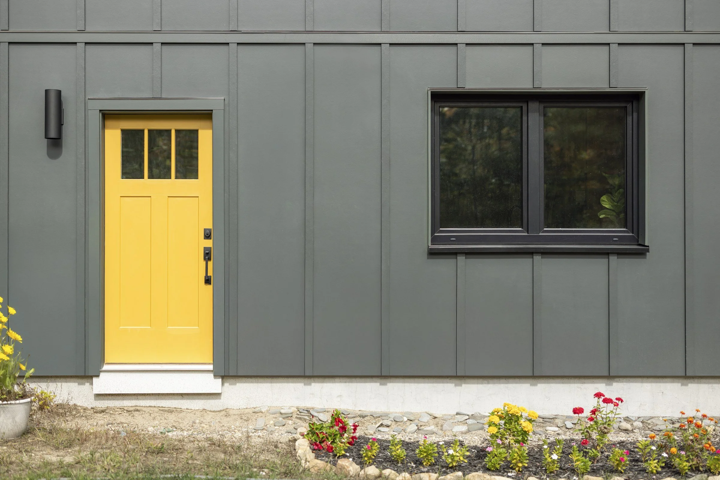 Yellow side-entry door and black-framed window set in dark board-and-batten siding.