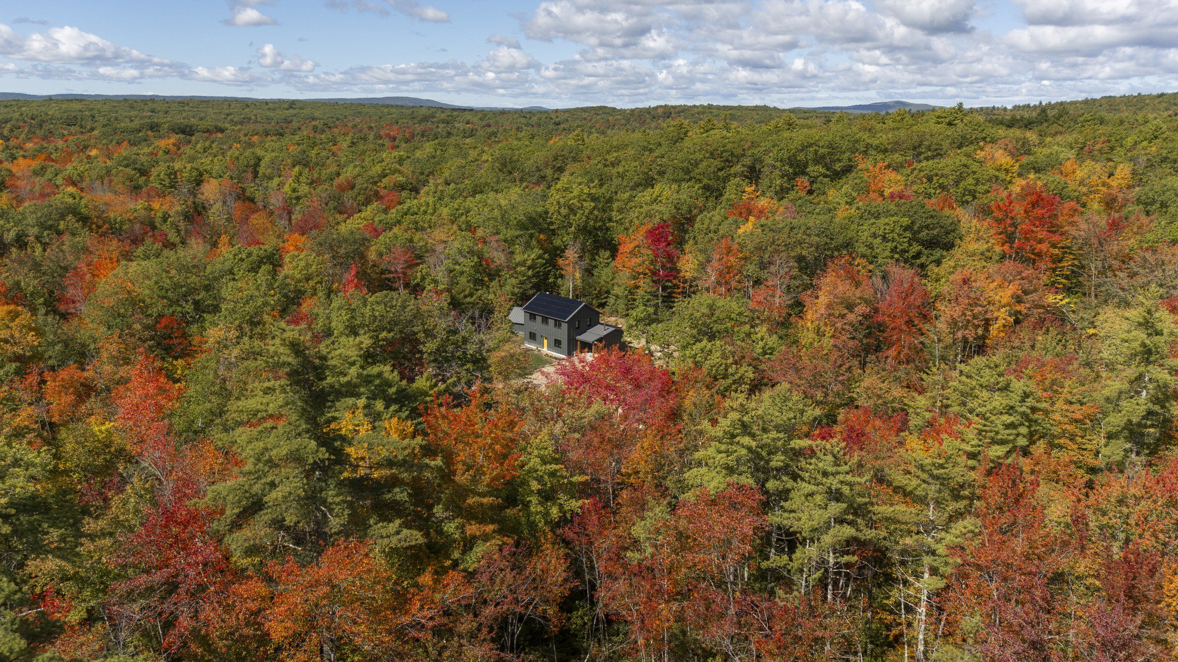 Wide aerial view of the off-grid Lyman home surrounded by autumn forest.