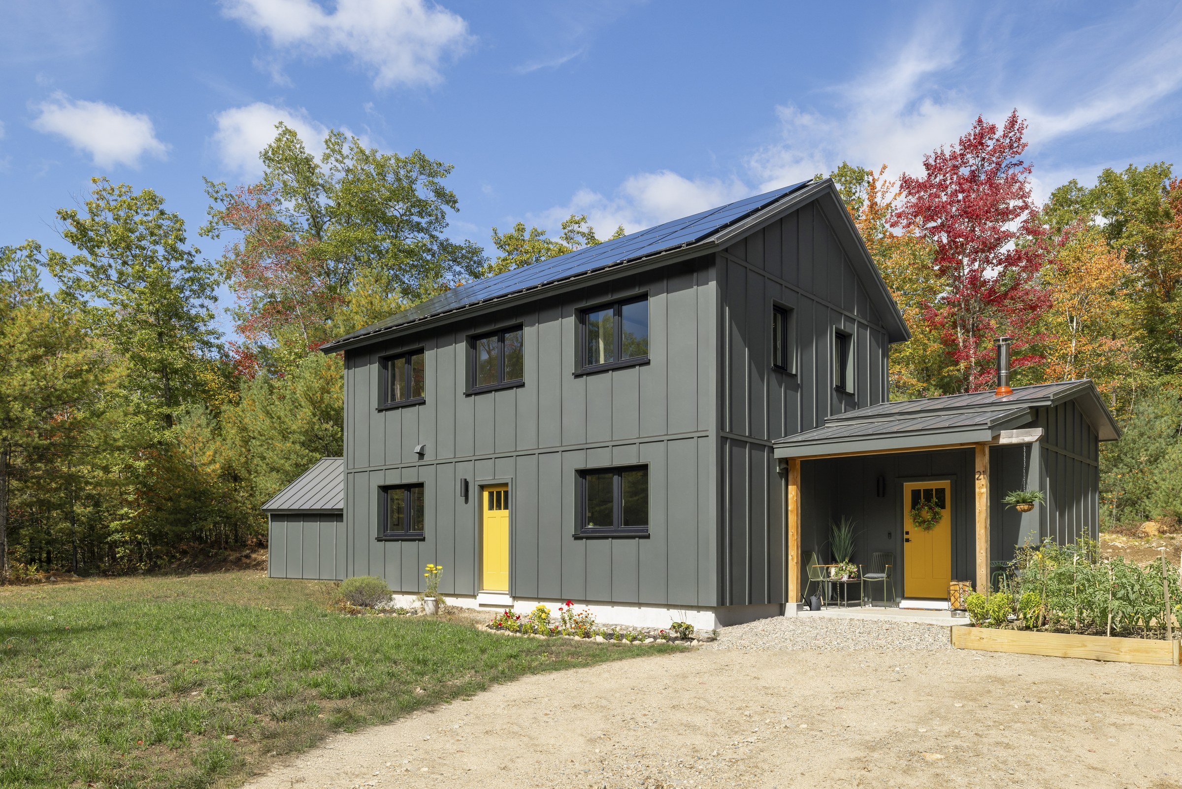 Lyman Residence exterior with dark siding, yellow entry doors, and a metal roof.