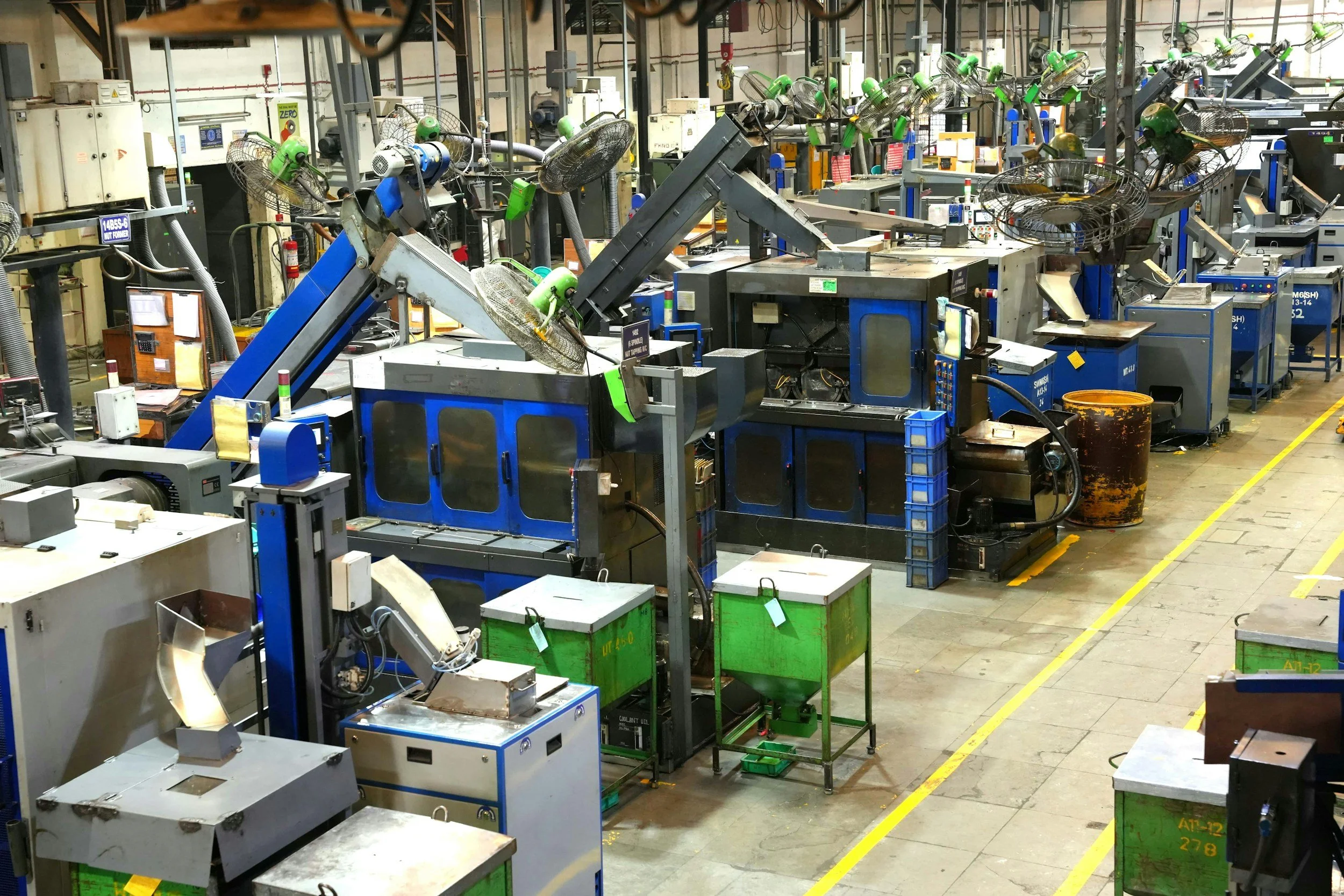 Industrial factory with multiple large blue and gray machines, robotic arms, and fans in a manufacturing setting.
