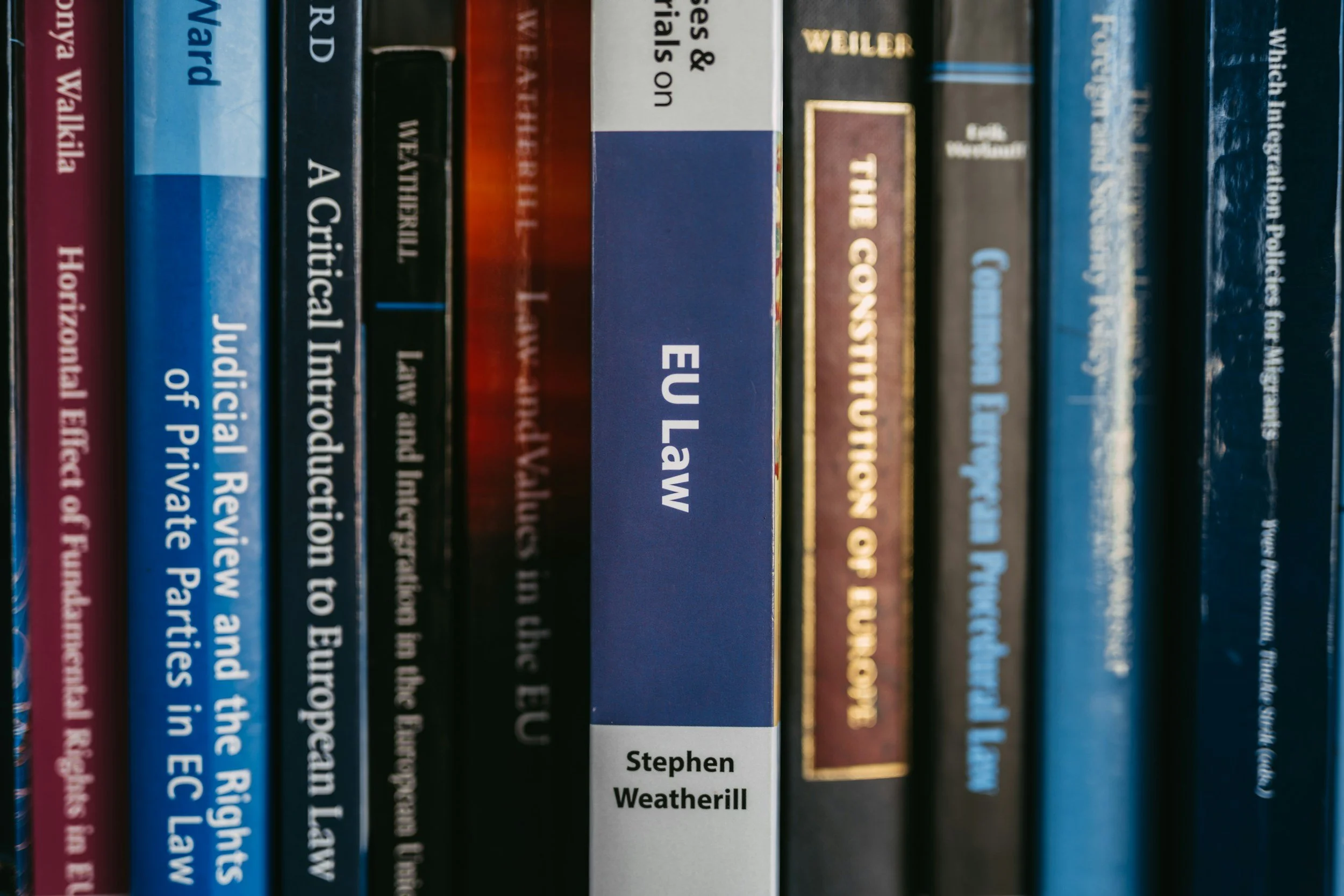Close-up of multiple books on a shelf, including 'EU Law' by Stephen Weatherill in the center, with titles related to law and politics visible.