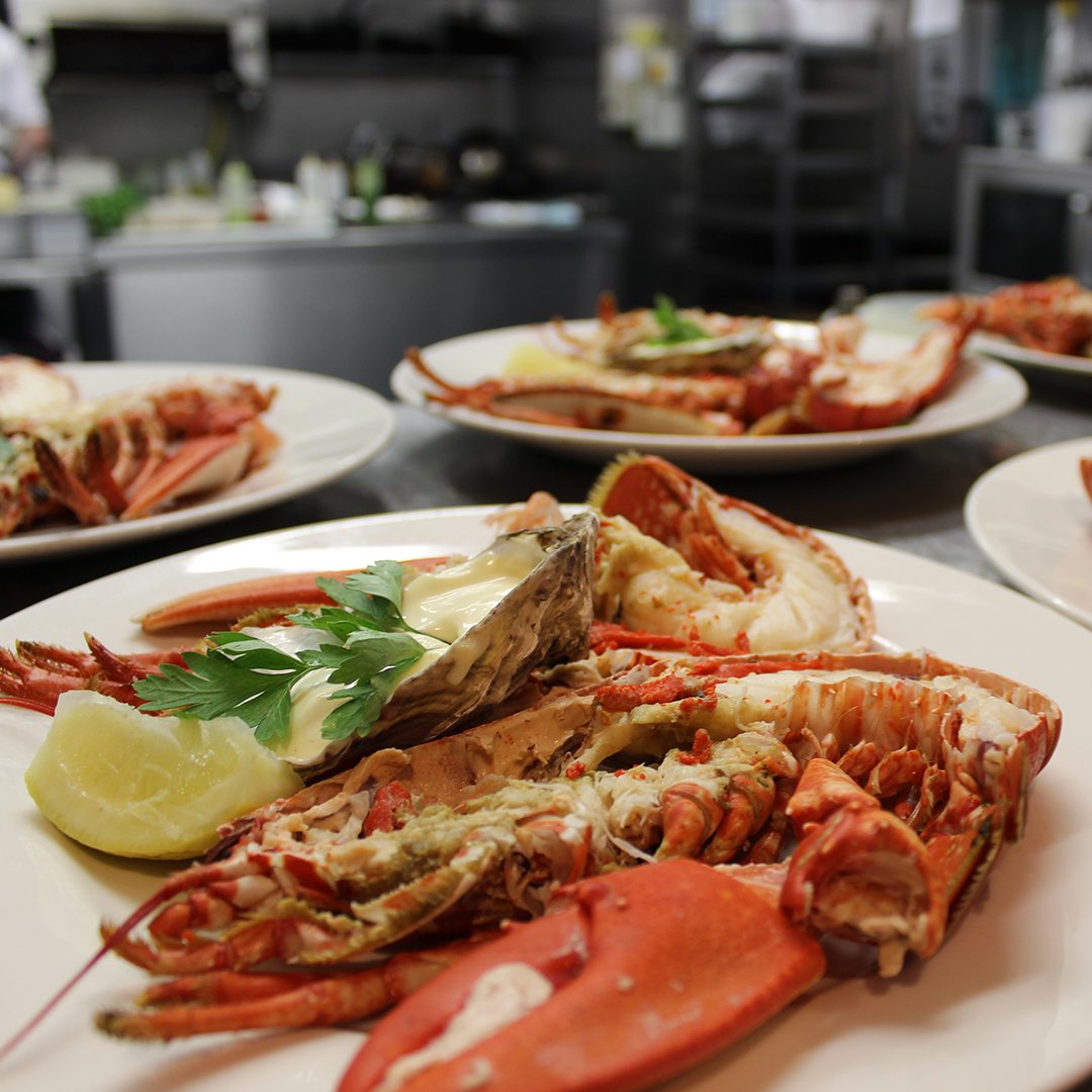 Plates of cooked lobster with garnishes in a kitchen setting.