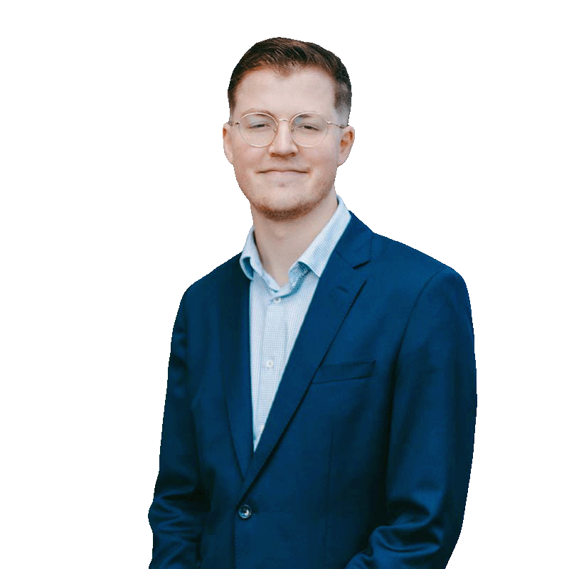 A young man with light skin, short hair, glasses, dressed in a blue suit jacket and a light blue shirt, standing against a white background with a slight smile.
