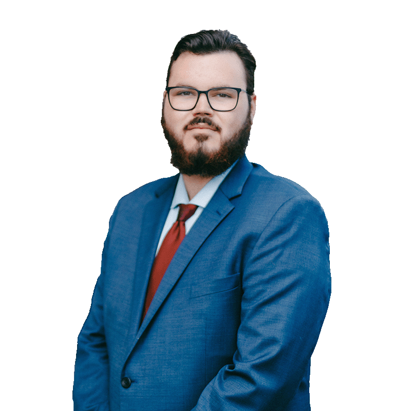 A man with a beard and glasses wearing a blue suit, white shirt, and red tie, standing against a white background.