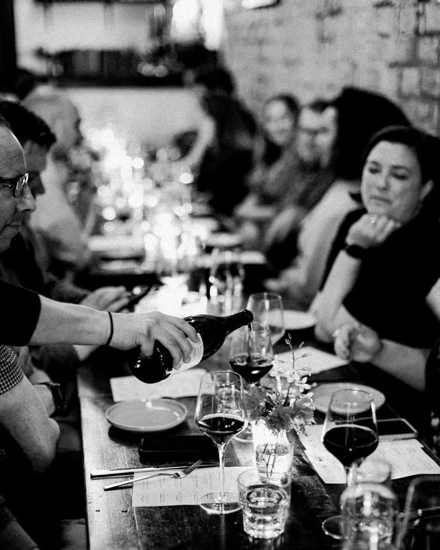 Patrons sit at a table on Field Bar + Bottle Shop in Tacoma. Wine is being poured. Photo is in black and white.