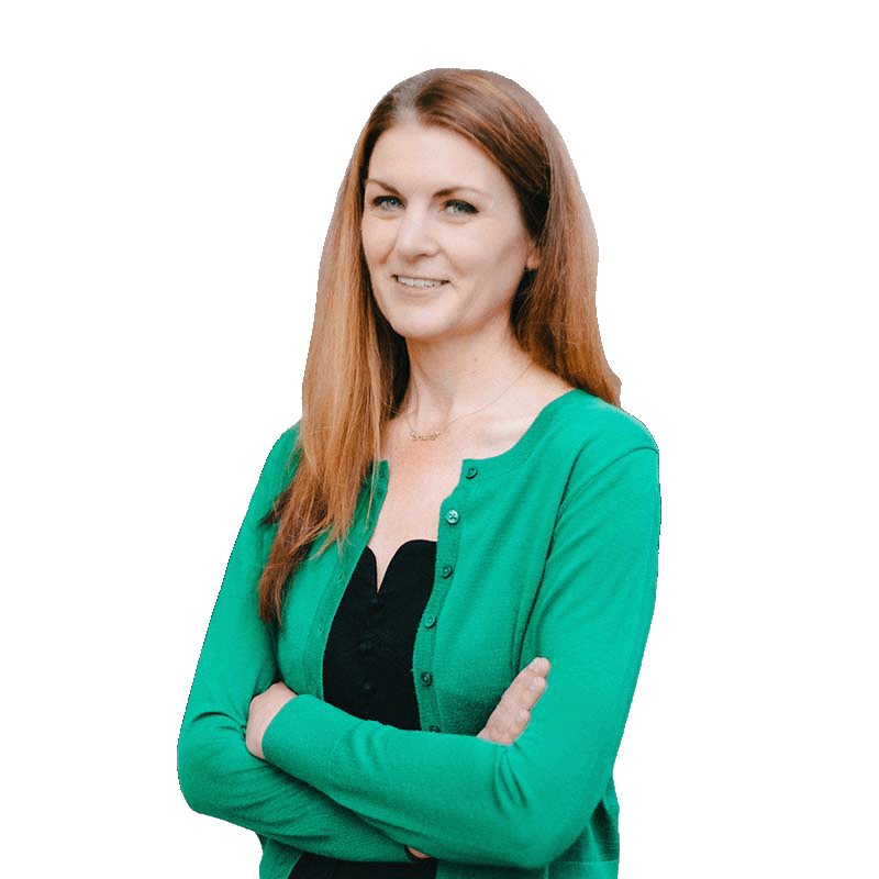 A woman with long brown hair wearing a green cardigan over a black top, standing with crossed arms against a white background.