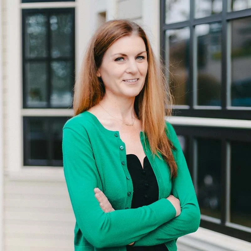 Smiling woman with long, brown hair in a black dress and green cardigan