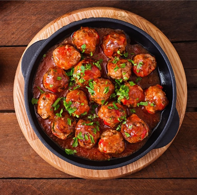 Meatballs in tomato sauce garnished with chopped parsley served in a cast iron skillet on a wooden board.
