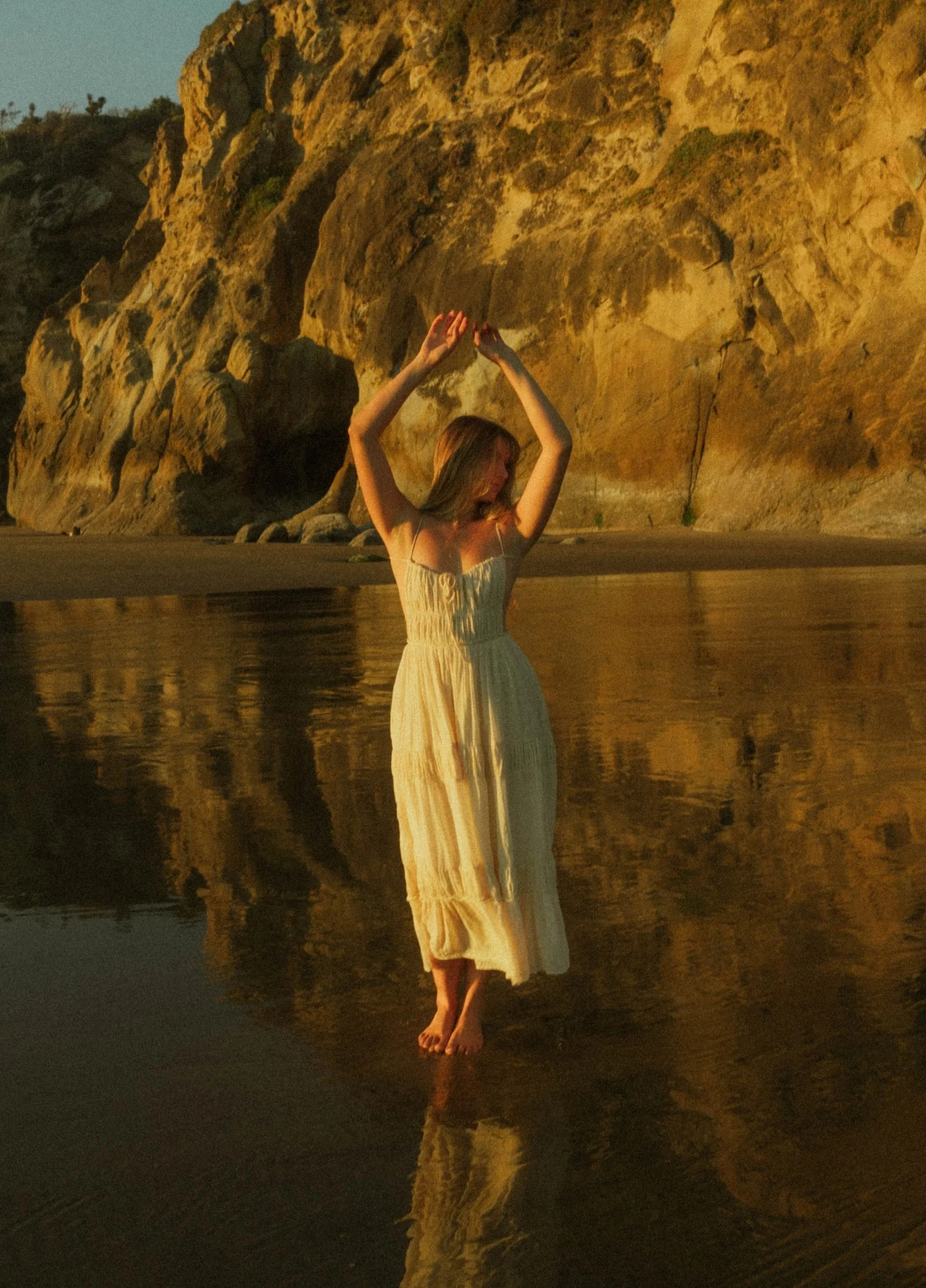 Woman in white dress standing at beach during sunset, cinematic portrait with soft natural light