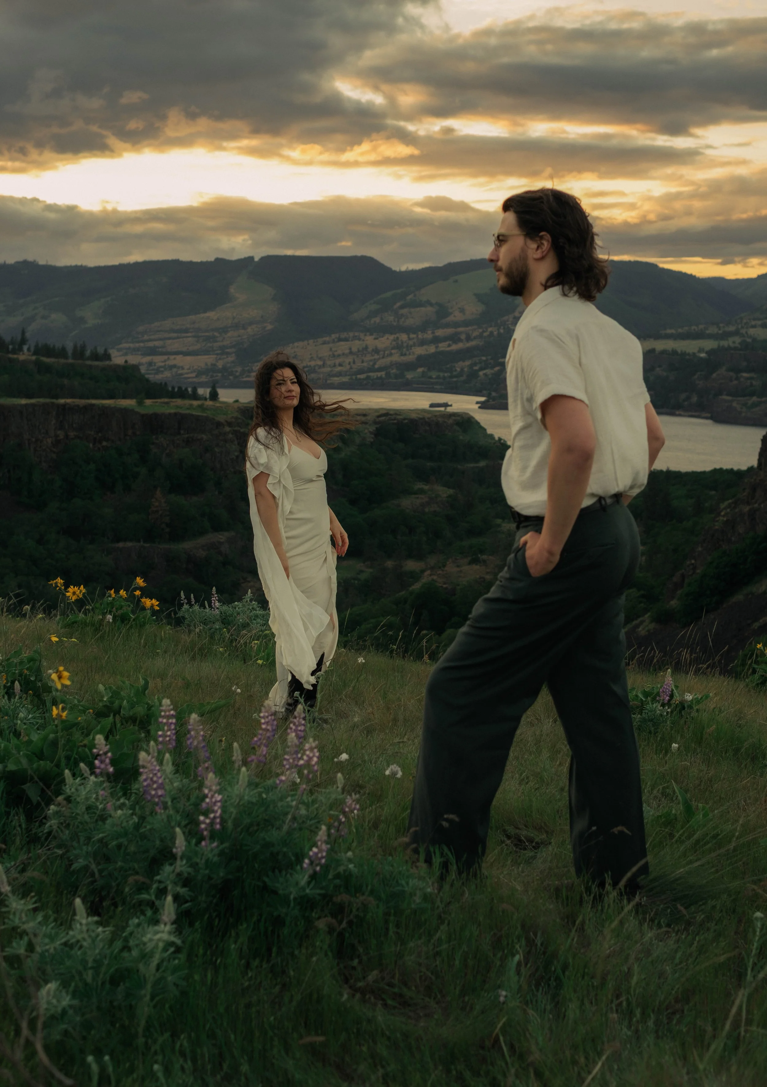Couple standing in wildflower field at sunset overlooking mountains and valley