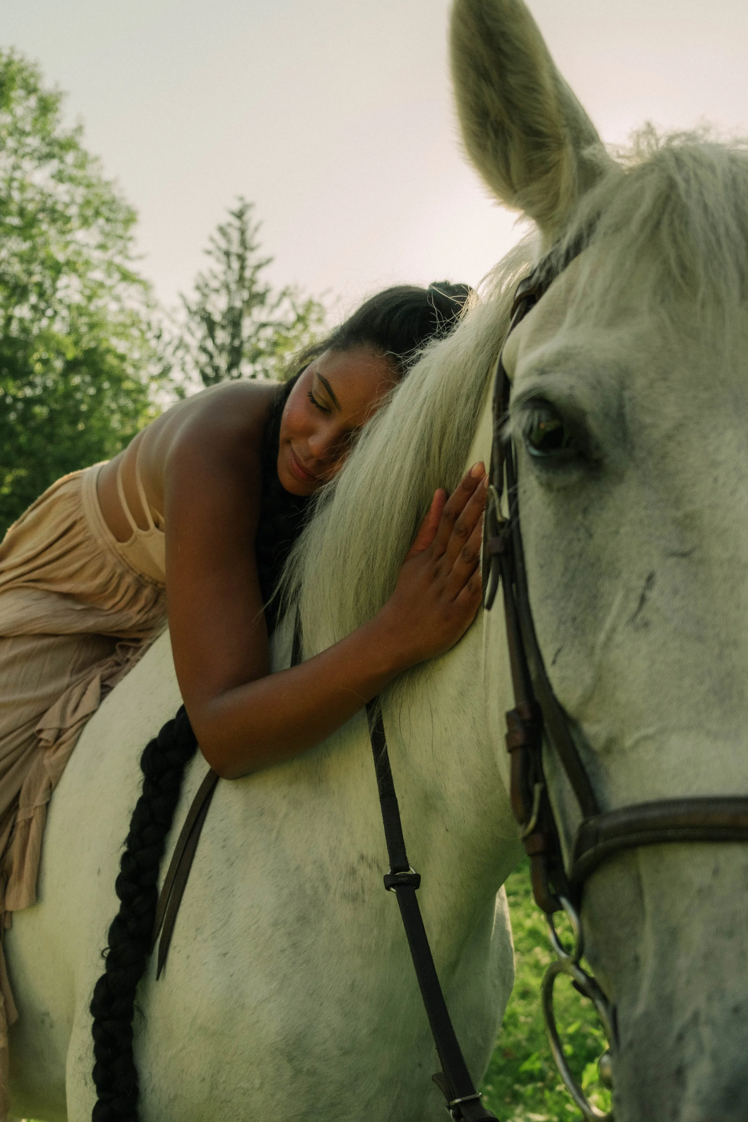 Woman gently resting her head against a white horse in a peaceful outdoor setting
