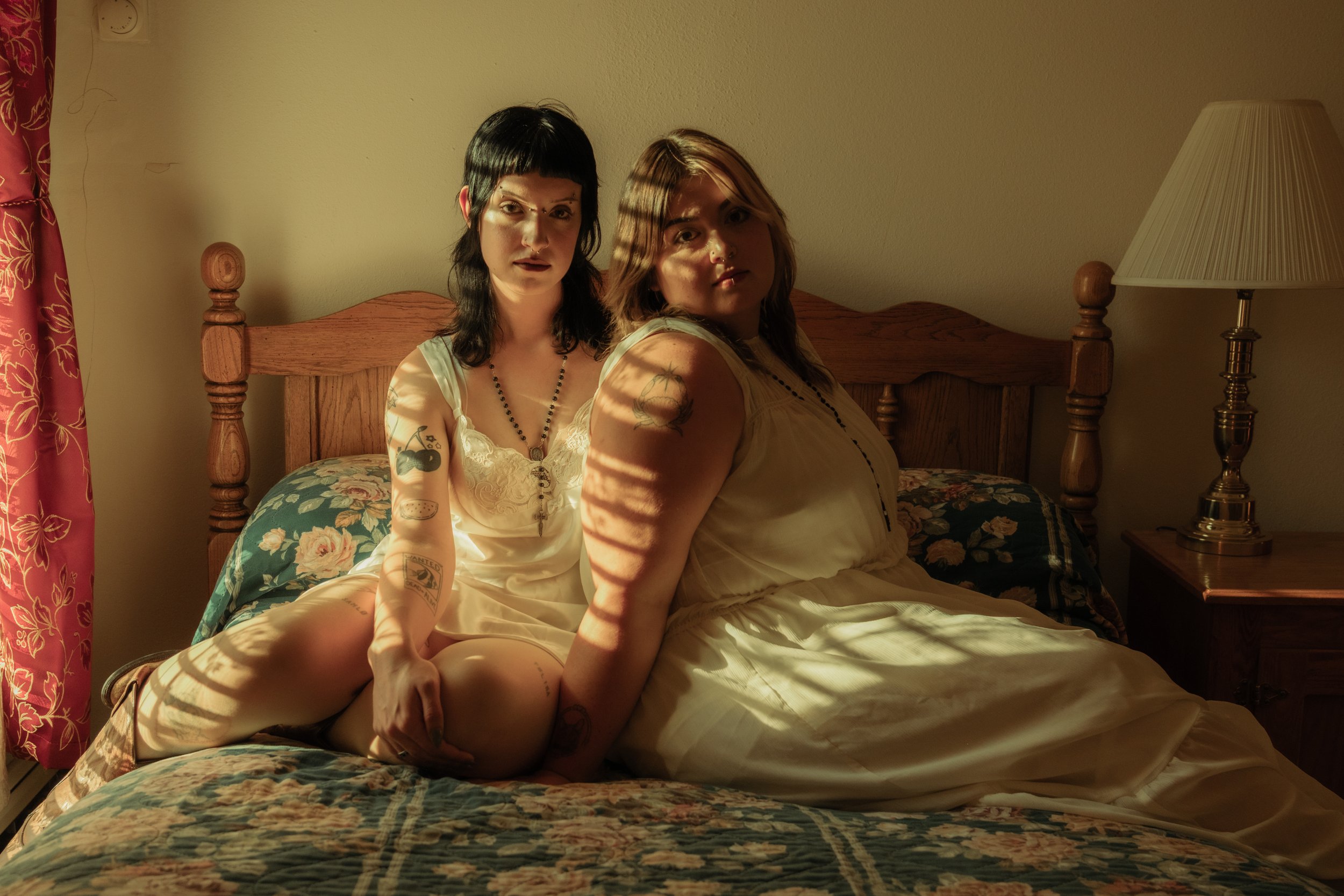 Two women sitting together on bed in warm window light, intimate lifestyle portrait