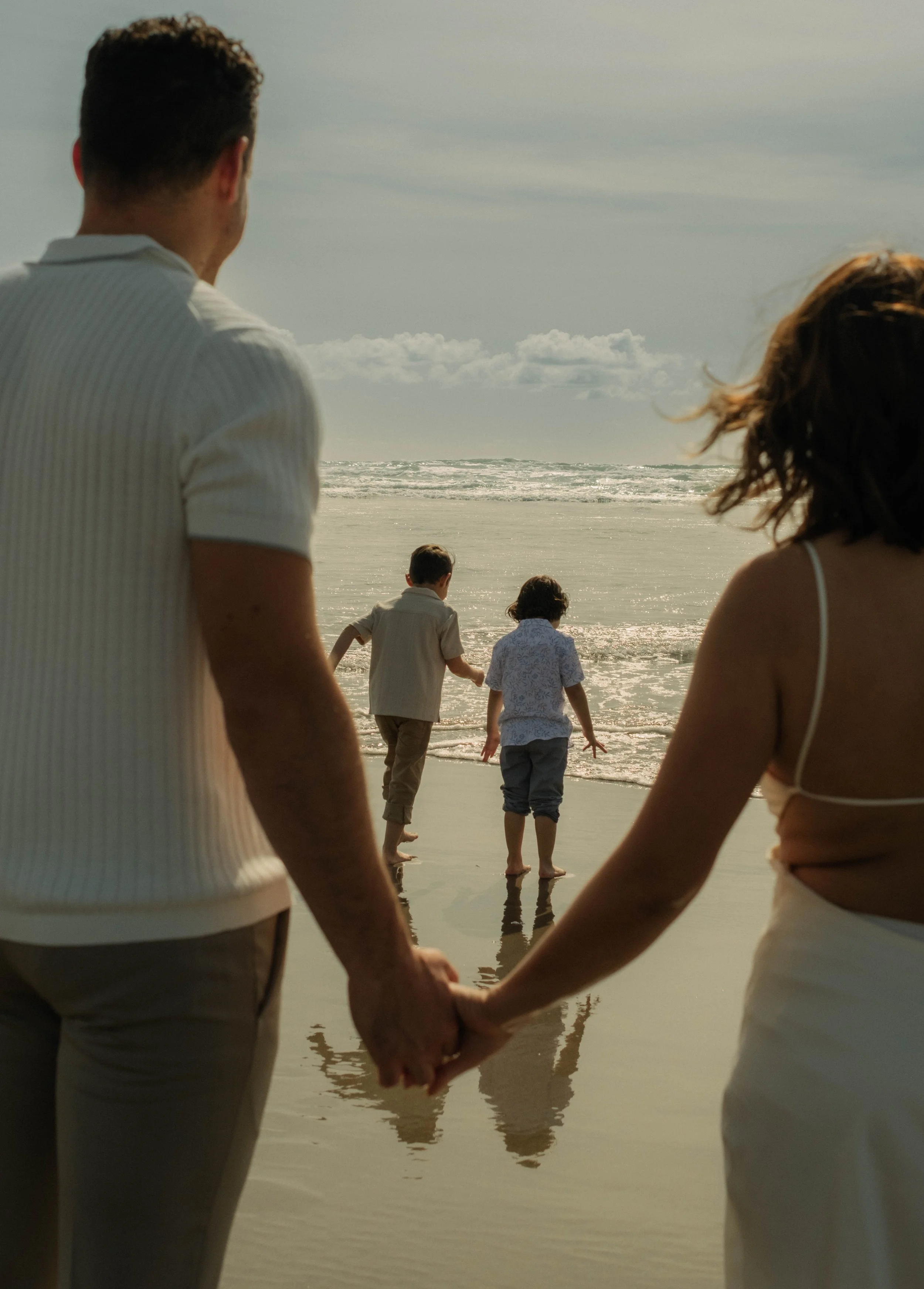 Family holding hands walking along the beach toward the ocean at sunset