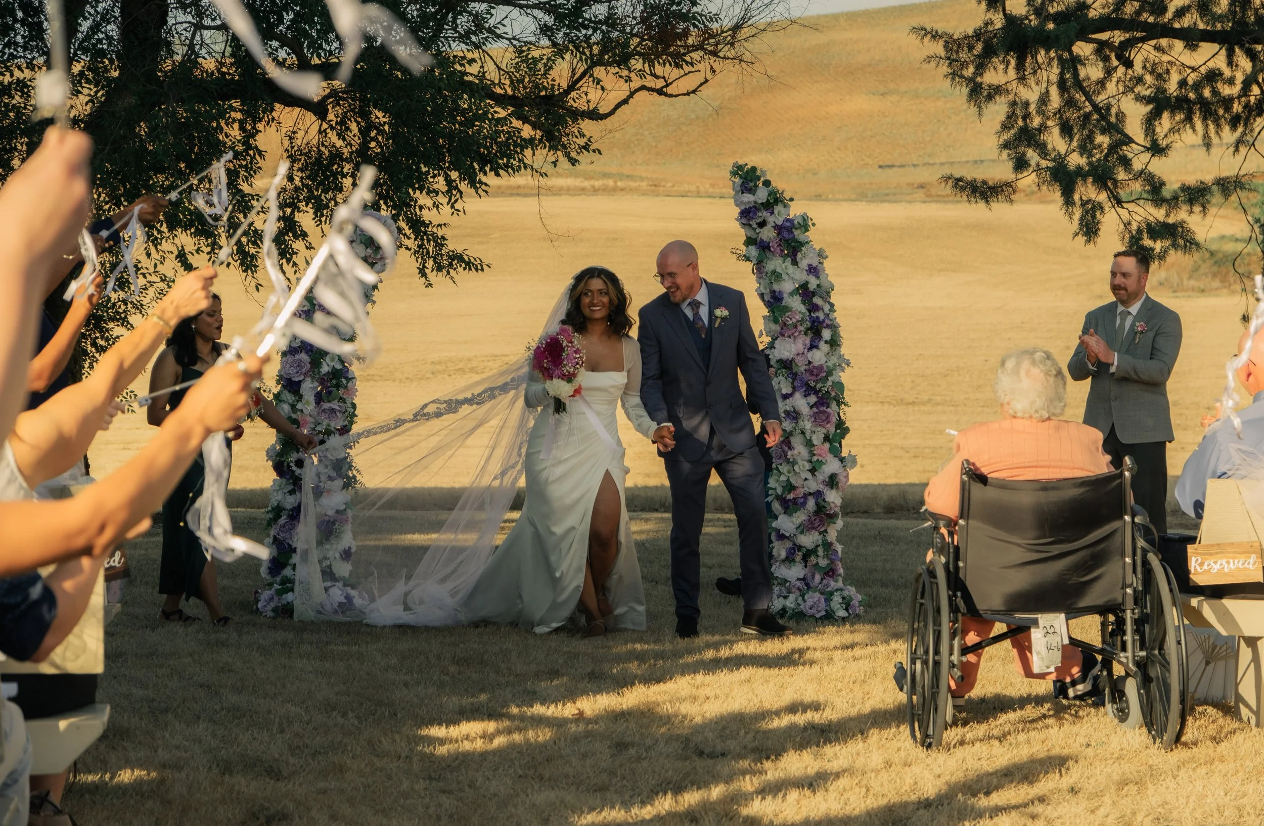 Wedding couple exiting ceremony arch outdoors, joyful moment with guests applauding