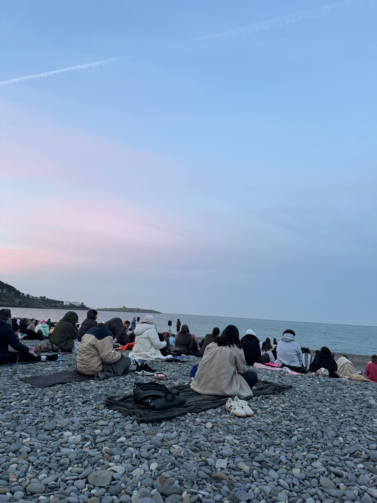 A group gathered by the sea for a quiet reflection session at dusk.