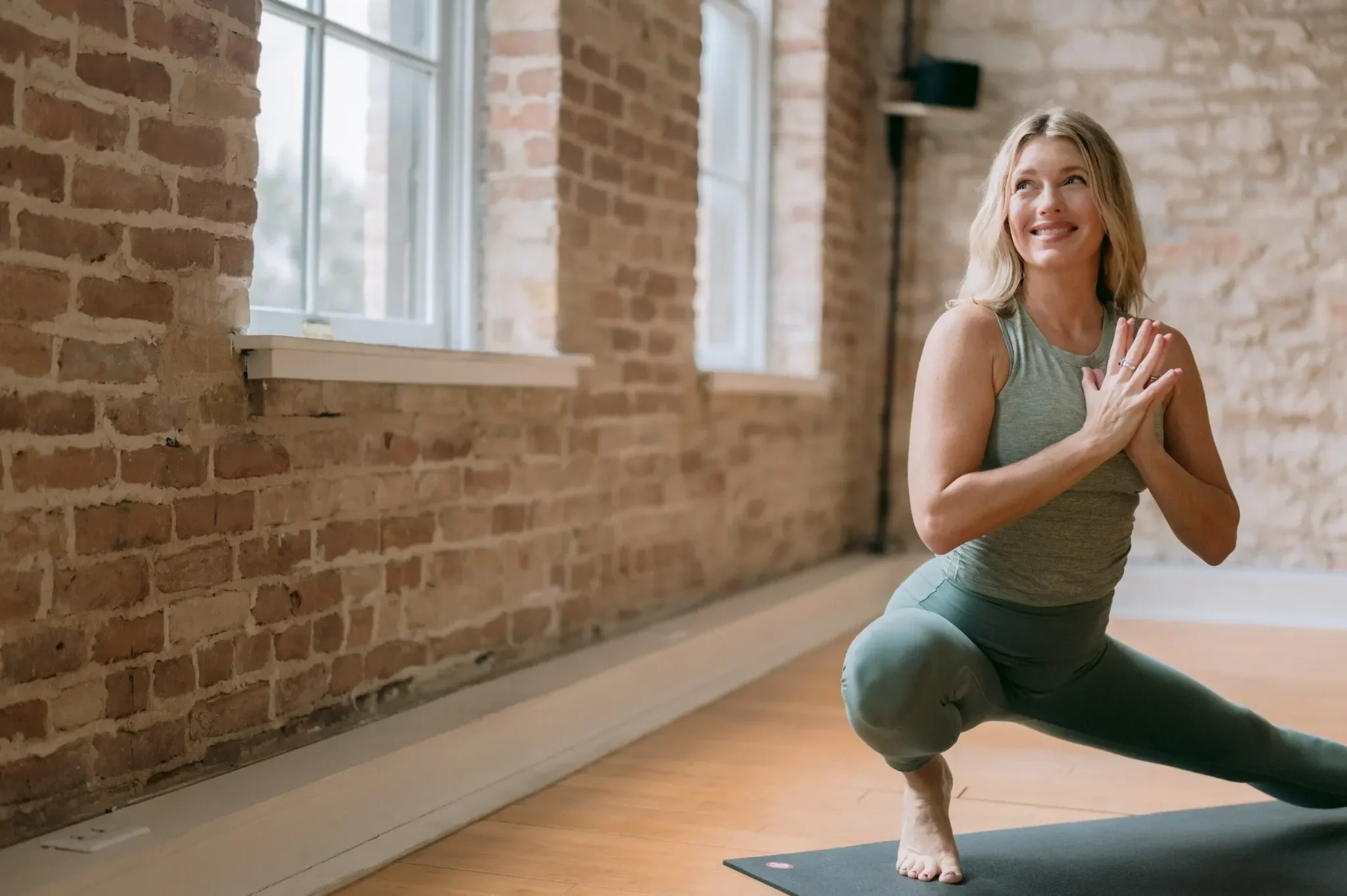 Woman practicing vinyasa flow yoga in a studio in Austin, holding a prayer lunge pose and smiling.