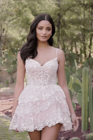 Model walking in Sherri Hill pink tiered lace mini dress with corset bodice and ruffle skirt.